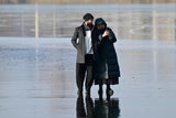 Zwei Personen auf dem Eis der Alten Donau – das Handy im Fokus, die Gefahr im Hintergrund. 