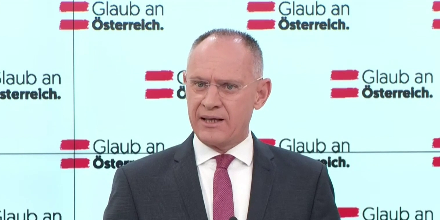 Eine Frau spricht bei einer Pressekonferenz vor dem österreichischen Nationalflagge.