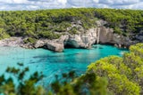 Cala Mitjana,&nbsp;ein feinkörniger Sandstrand, der von Felsen und Bäumen umgeben ist.
