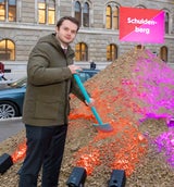 Zierfuß steht vor einem rot-pinken Schulden, fährt aber Audi A6. 