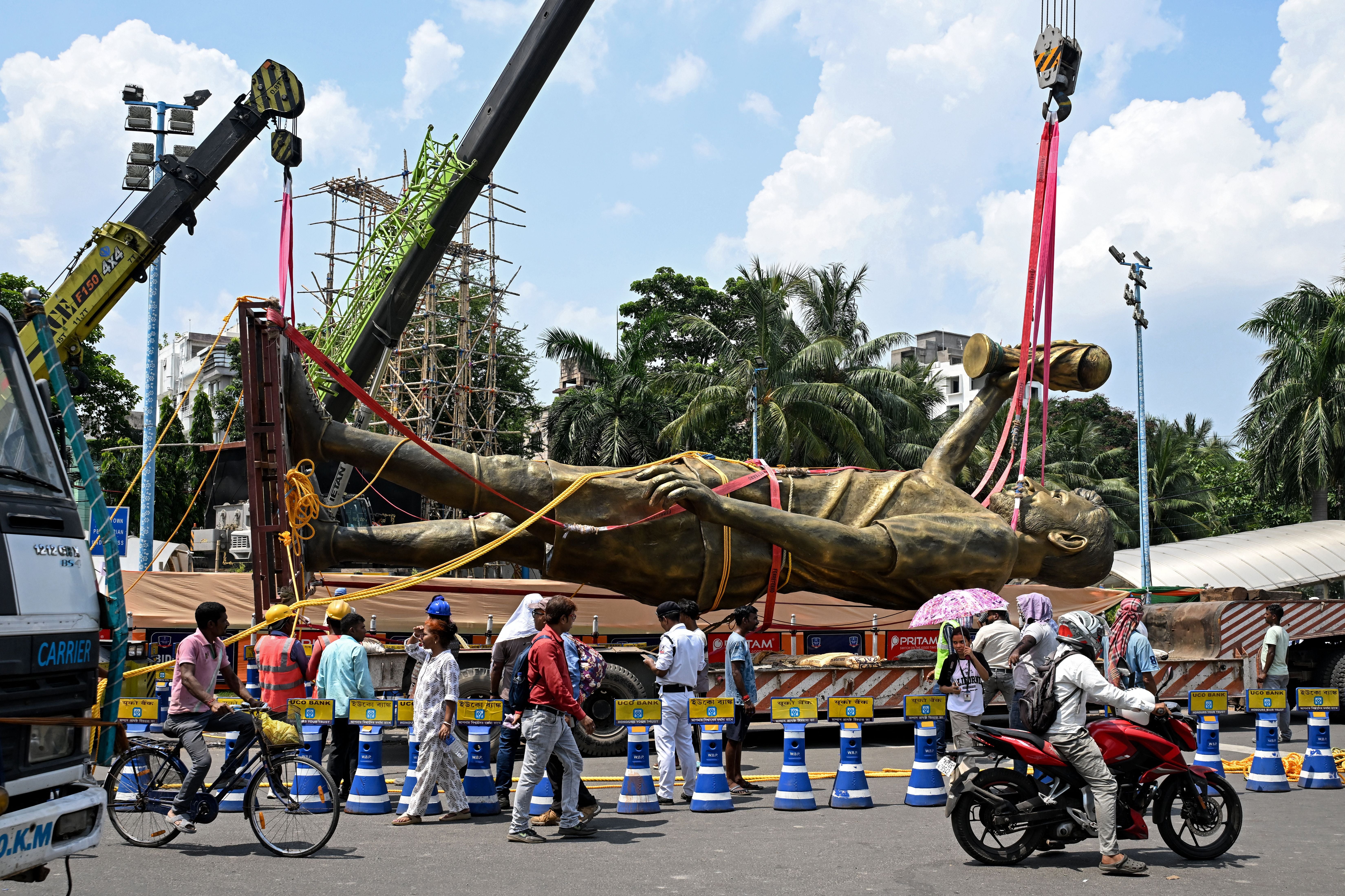 TOPSHOT - Pedestrians watch as workers remove a statue of Argentine football player Lionel Messi for its re-installation to a safer place in Kolkata on June 1, 2026. A giant statue of football superstar Lionel Messi erected in India to mark his visit last year is 'swaying in the wind' and will be removed, a lawmaker told AFP on May 27. (Photo by Dibyangshu SARKAR / AFP)