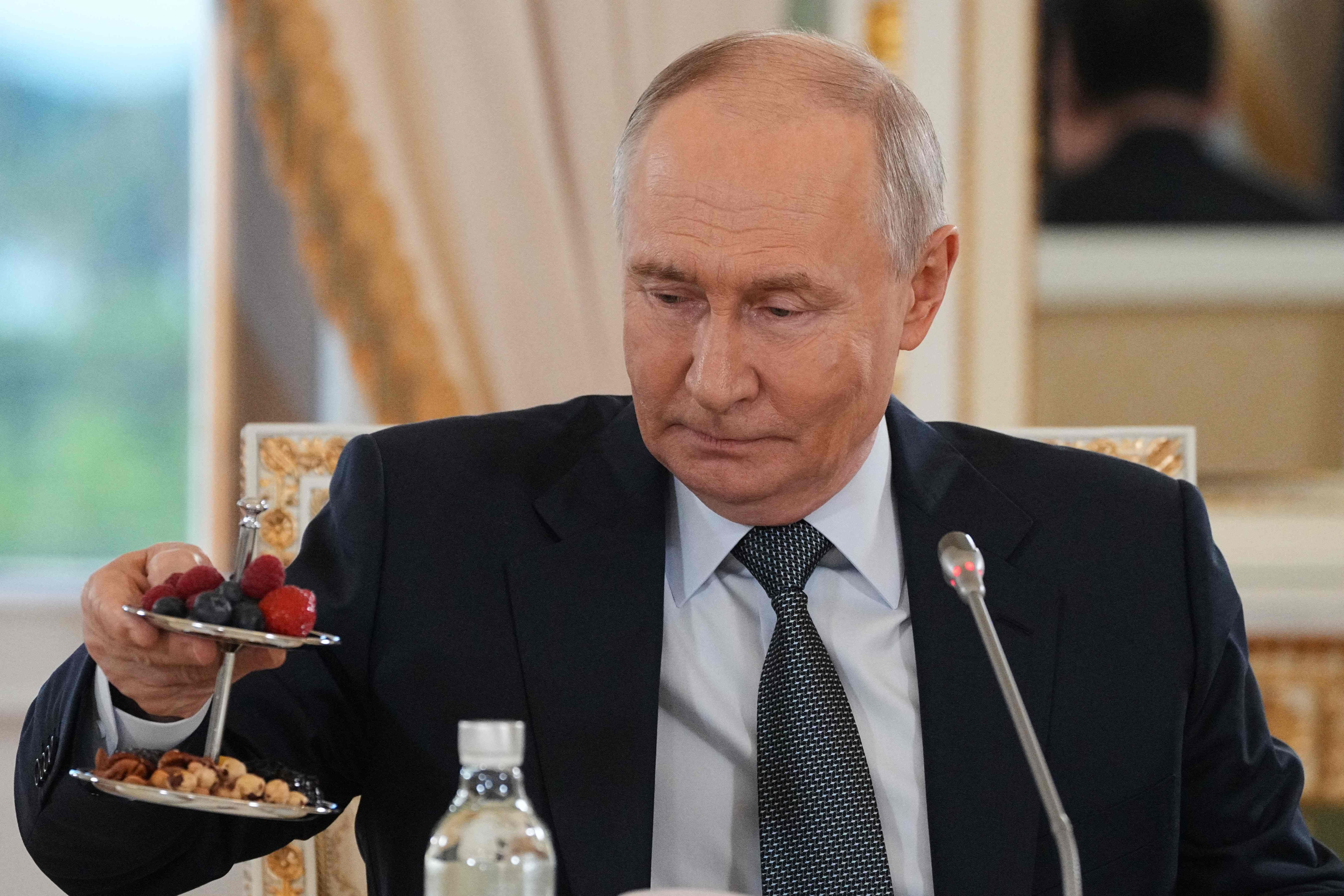 Russian President Vladimir Putin takes a dessert as he arrives to meet with representatives of international news agencies on the sidelines of the St. Petersburg International Economic Forum at the Constantine Palace in Saint Petersburg on June 4, 2026. (Photo by Dmitry LOVETSKY / POOL / AFP)