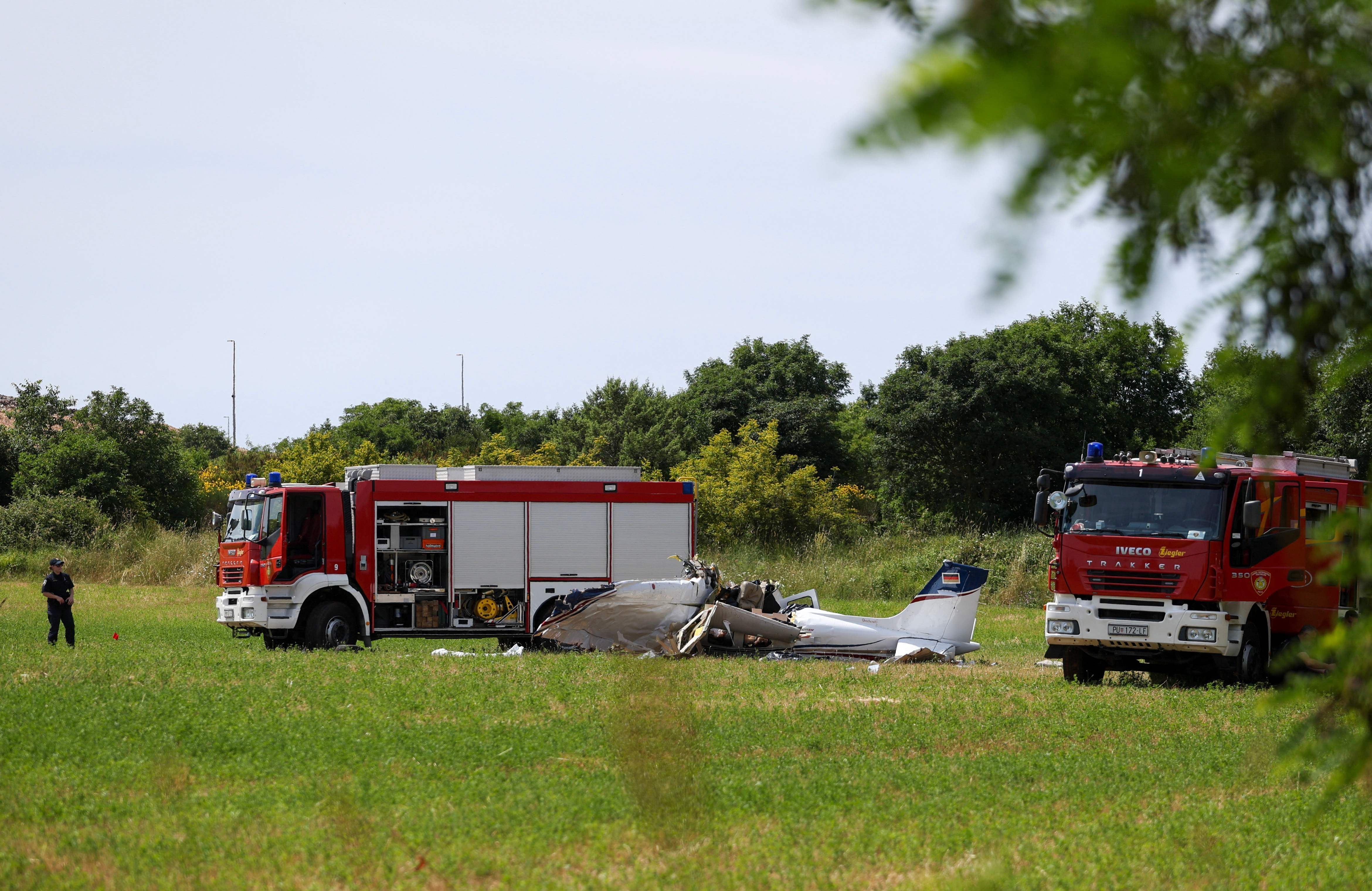 A police officer and firetrucks are seen at site of a small plane crash, which killed 4 people, in Medulin on Croatia's northern Adriatic coast, on June 4, 2026. The accident occurred in the Campanoz area, outside the town, and 'all emergency services are on the scene'. According to the state-run HRT broadcaster, it was a small aircraft registered in Germany, which had taken off from Austria with Medulin as its destination. (Photo by AFP)