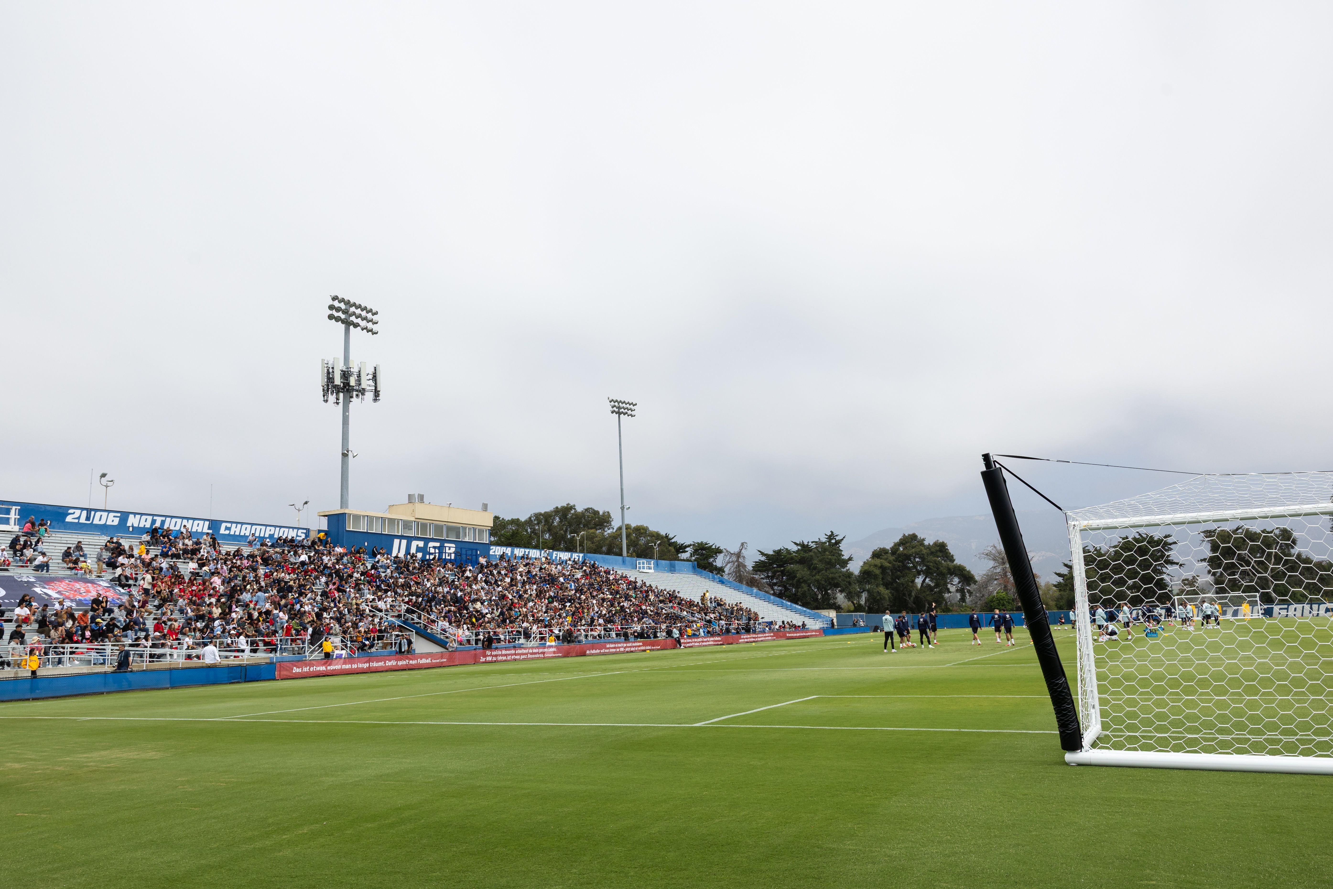 Ein saftig grüner Fußballplatz im Harder Stadium in Santa Barbara mit einer gut gefüllten Tribüne im Hintergrund unter einem dicht bewölkten Himmel, im Vordergrund ist ein mobiles Tor zu sehen. Etwa 3.000 Fans ließen sich den ersten lockeren Aufgalopp der ÖFB-Auswahl nicht entgehen