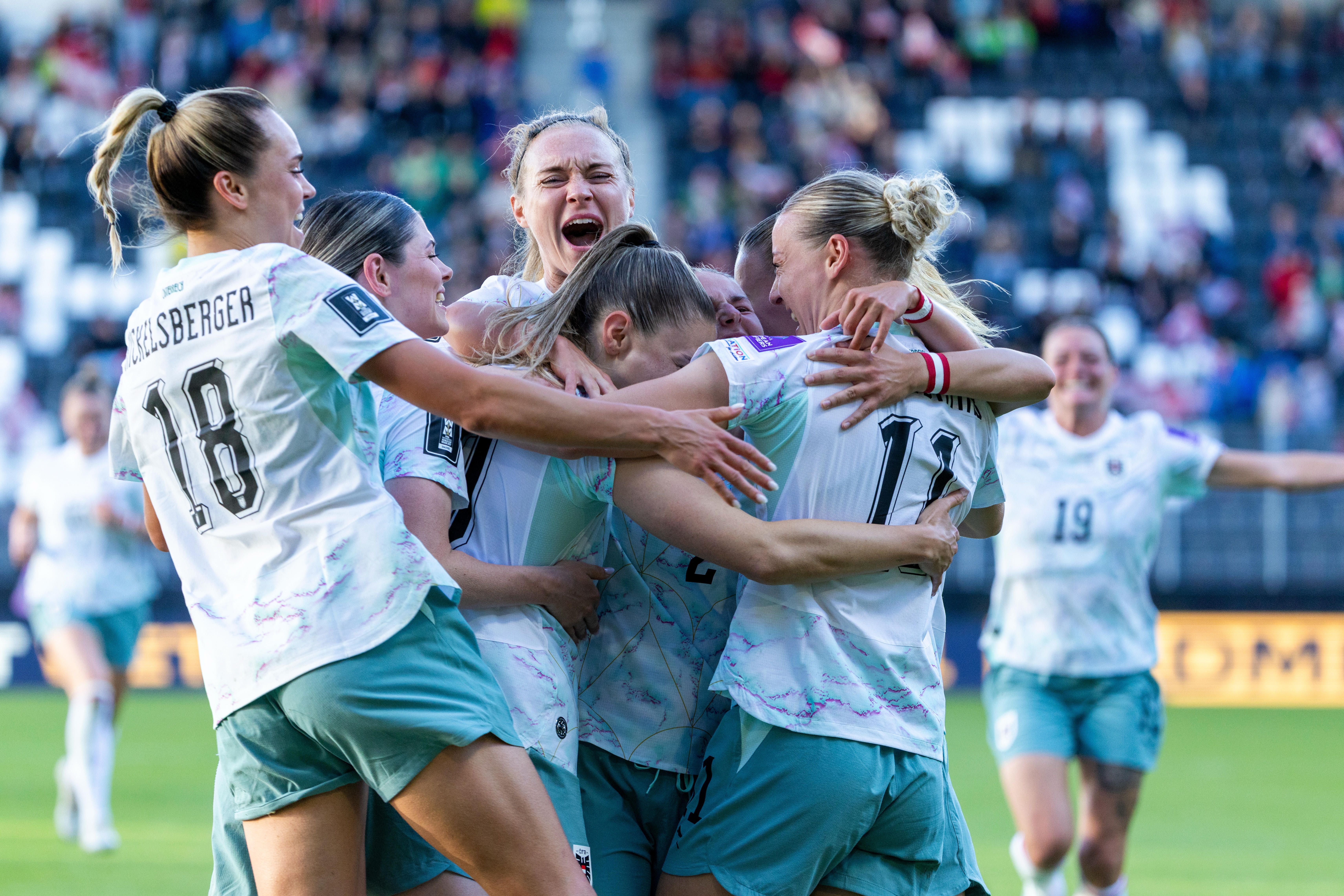 Mehrere Spielerinnen des österreichischen Frauen-Nationalteams im Fußball liegen sich jubelnd in den Armen. Im Vordergrund trägt eine Spielerin die Rückennummer 18 und den Namen Hickelsberger. Die Spielerinnen tragen weiße Trikots und hellblaue Hosen. Im Hintergrund ist eine gut gefüllte Stadiontribüne zu sehen.