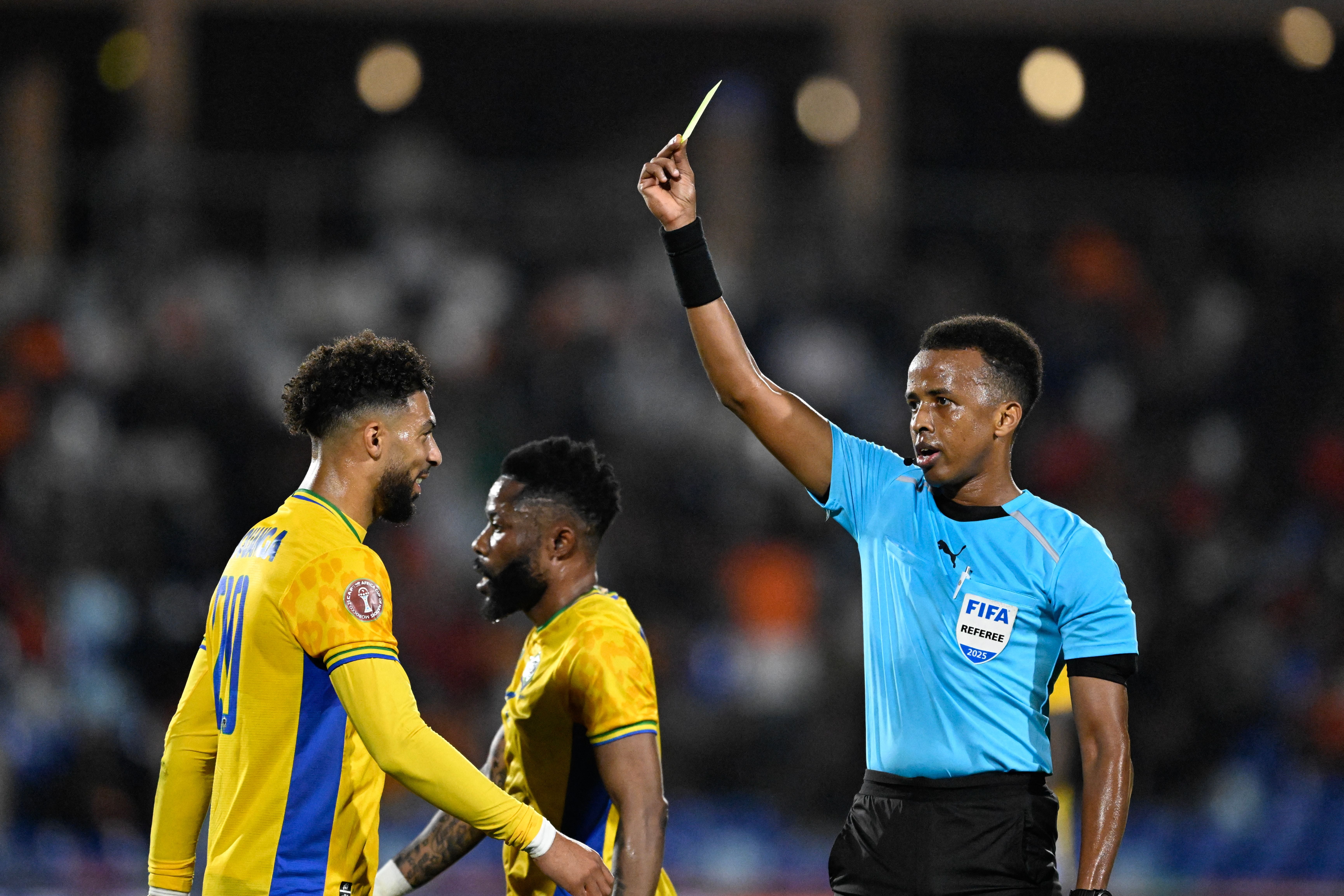 (FILES) Gabon's forward #20 Denis Bouanga is shown the yellow card by Somali referee Omar Abdulkadir Artan during the Africa Cup of Nations (CAN) Group F football match between Gabon and Ivory Coast at the Grand Stadium in Marrakech on December 31, 2025. Award-winning Somali referee Omar Artan, set to be the first from his country to officiate at the World Cup, was denied entry to the United States, a sports ministry official told AFP on June 8, 2026. 'Denying him entry to the United States and preventing him from officiating scheduled matches harms not only him personally but also undermines football's commitment to fairness, merit, and the spirit of fair play,' Ciise Aden Abshir, a senior advisor to Somalia's Ministry of Youth and Sports and a former national team captain, told AFP. (Photo by Khaled DESOUKI / AFP)