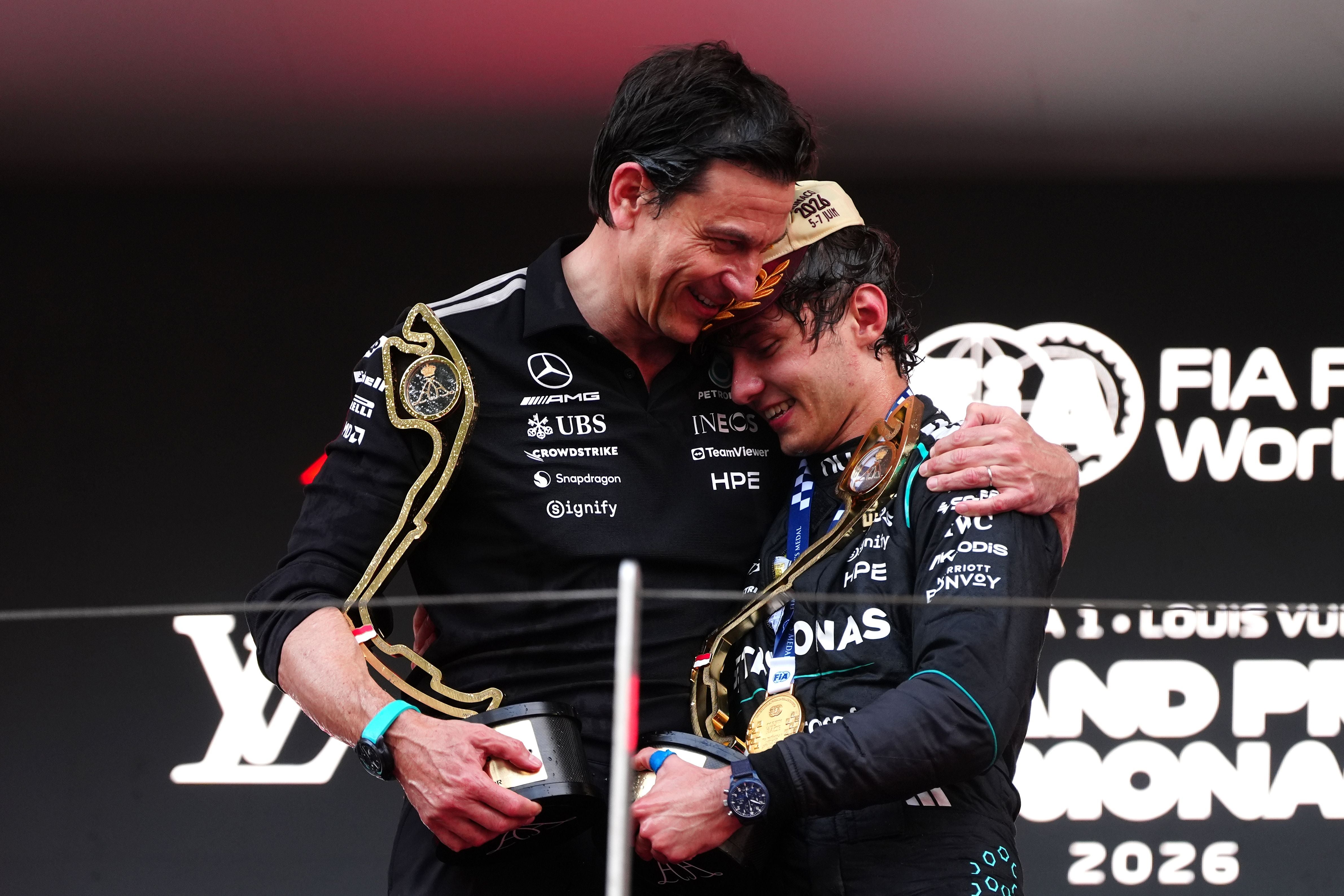 Mercedes-Motorsportchef Toto Wolff umarmt Kimi Antonelli auf dem Podium beim Großen Preis von Monaco 2026, beide halten Trophäen in den Händen und lächeln.