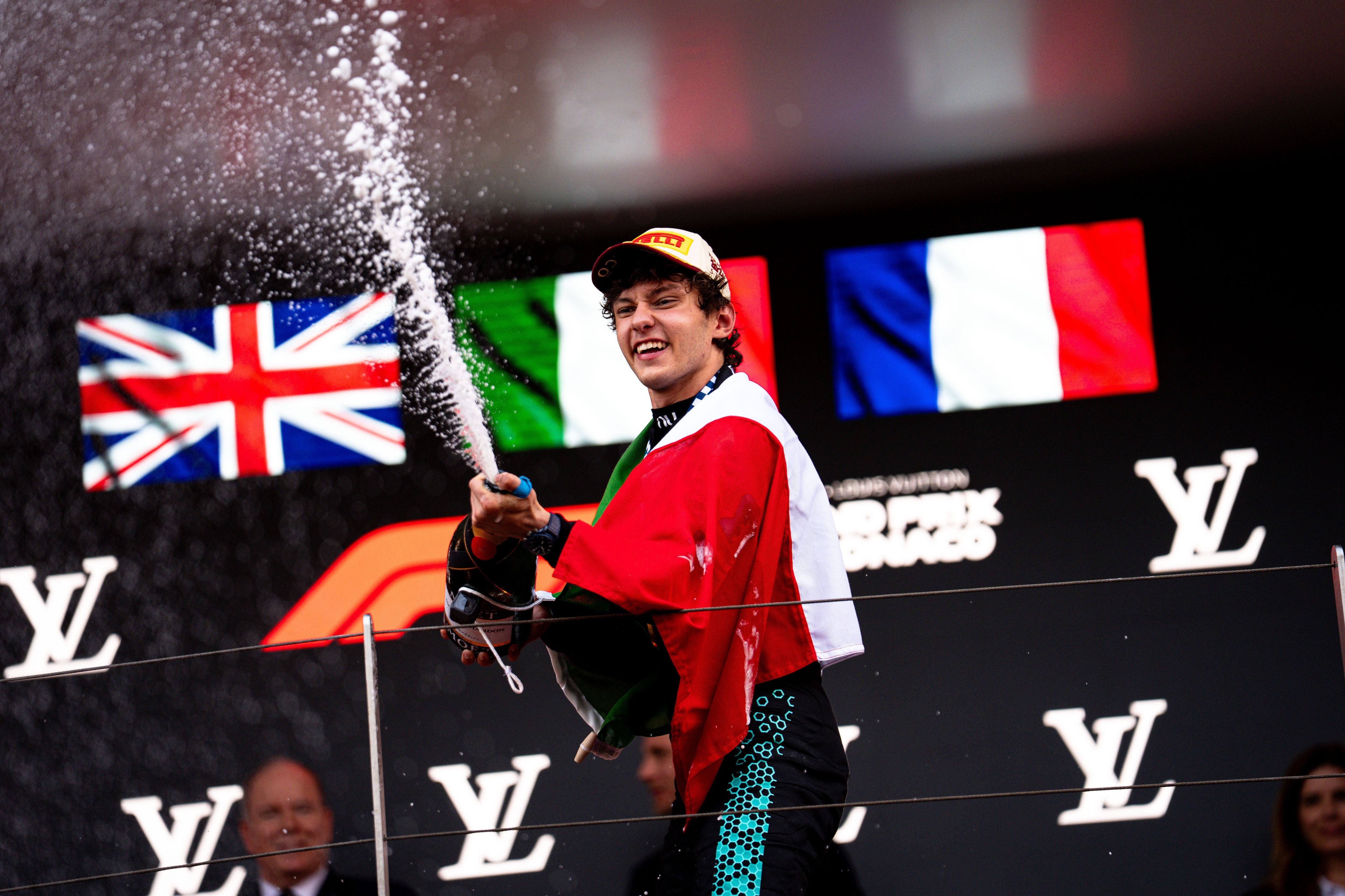 Kimi Antonelli steht lächelnd auf dem Siegerpodest beim Großen Preis von Monaco 2026, trägt eine Flagge über den Schultern und spritzt mit einer Champagnerflasche.