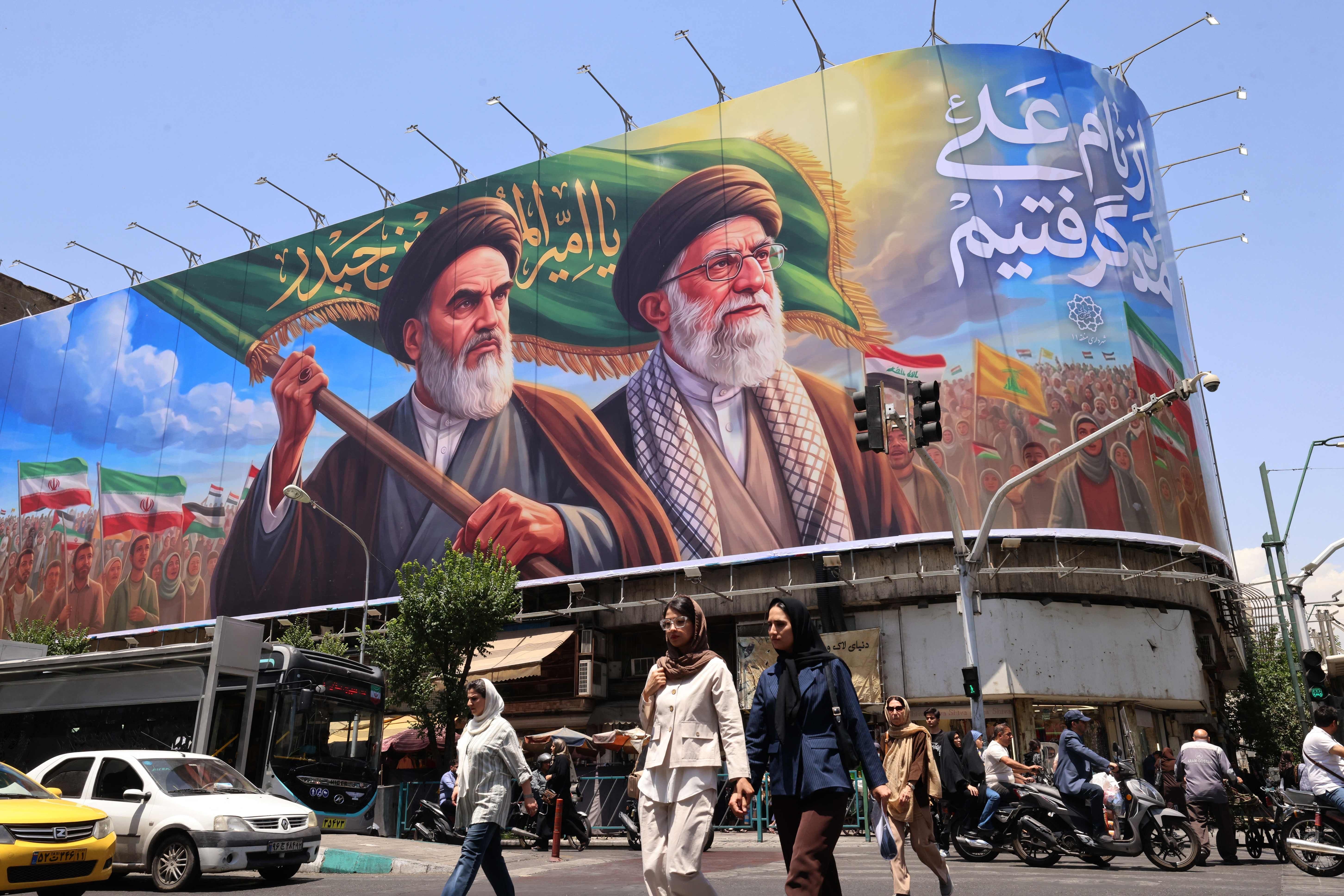 TOPSHOT - People cross the street past a large billboard showing portraits of Iran's late supreme leader, Ayatollah Ruhollah Khomeini (L) and slain supreme leader Ayatollah Ali Khamenei (R) in central Tehran on June 8, 2026. Iran said on June 8 that the resumption of hostilities in the Middle East war will have consequences for ongoing talks with the United States to reach peace in the region. 'It is perfectly natural that the diplomatic process initiated to put an end to this imposed war would be affected,' Iranian foreign ministry spokesman Esmaeil Baqaei said at a press conference in Tehran. (Photo by ATTA KENARE / AFP) /