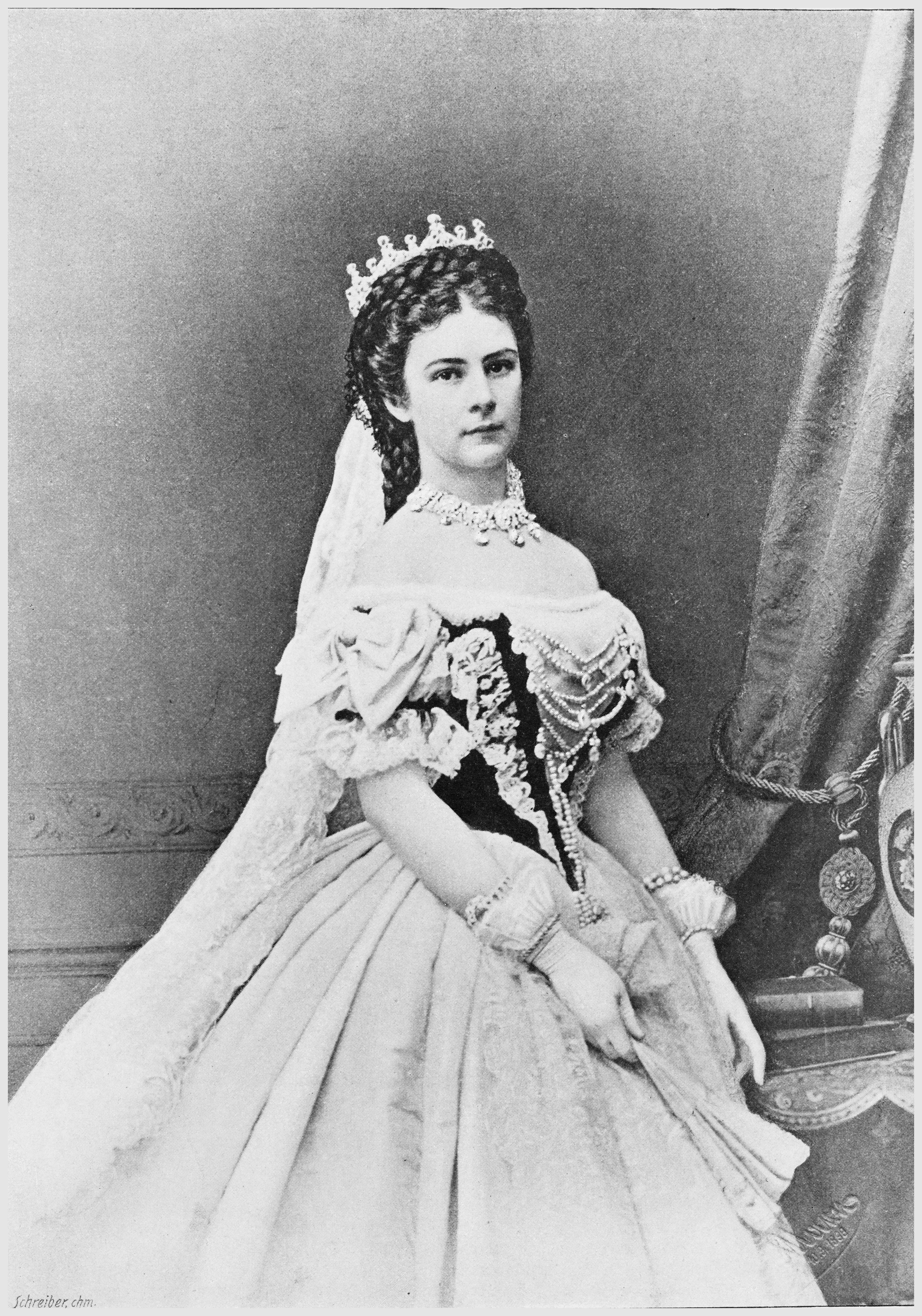 A formal black and white photographic portrait of Empress Elisabeth of Austria, depicted full-length in an elaborate gown, crown, and jewelry. This 19th-century studio photograph captures her regal presence and intricate attire.