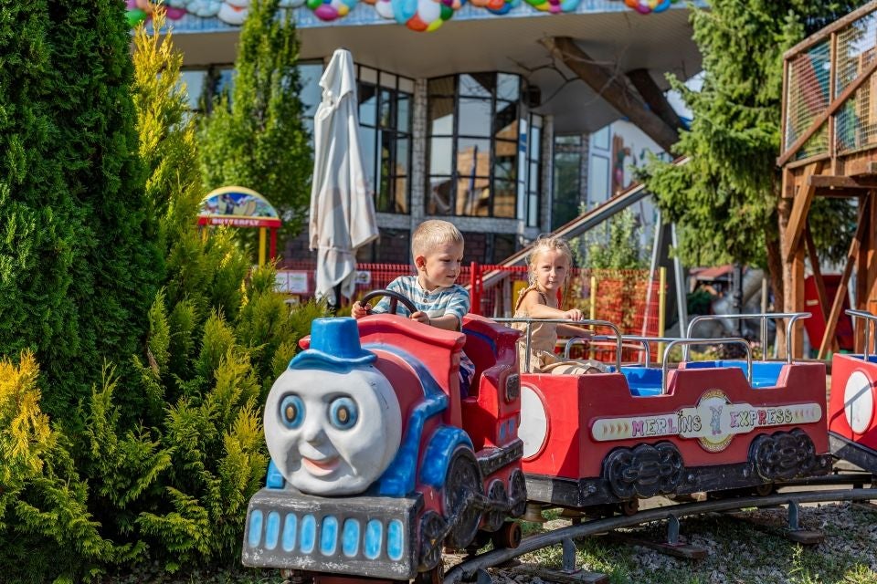 Zwei Kinder fahren mit dem kleine Zug "Thomas, die Lokomotive" durch Merlin's Kinder in der Family City.