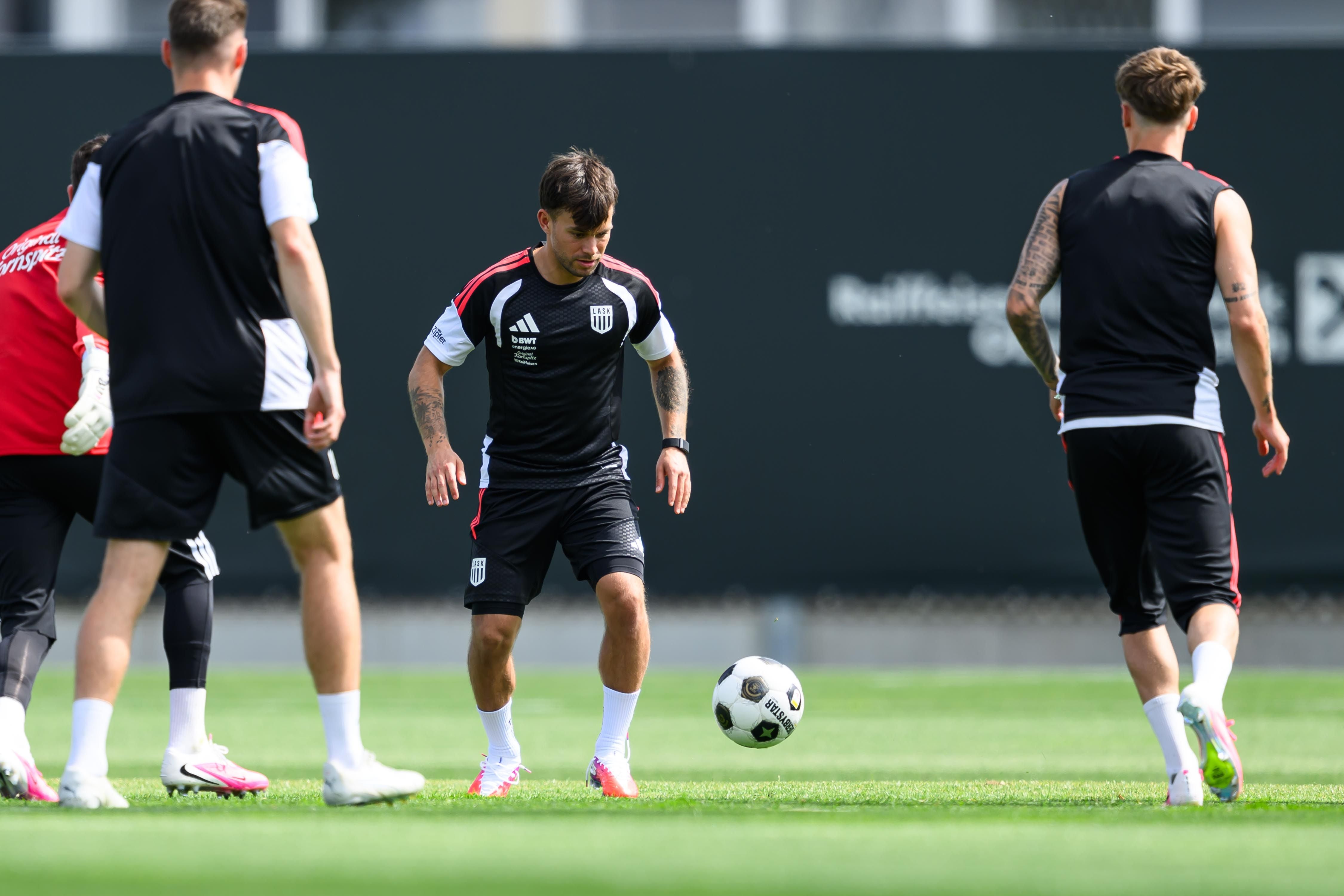LASK-Kapitän Sascha Horvath kontrolliert im schwarzen Trainingsgewand konzentriert den Fußball am Fuß, während seine Teamkollegen die Szene im Training beobachten.