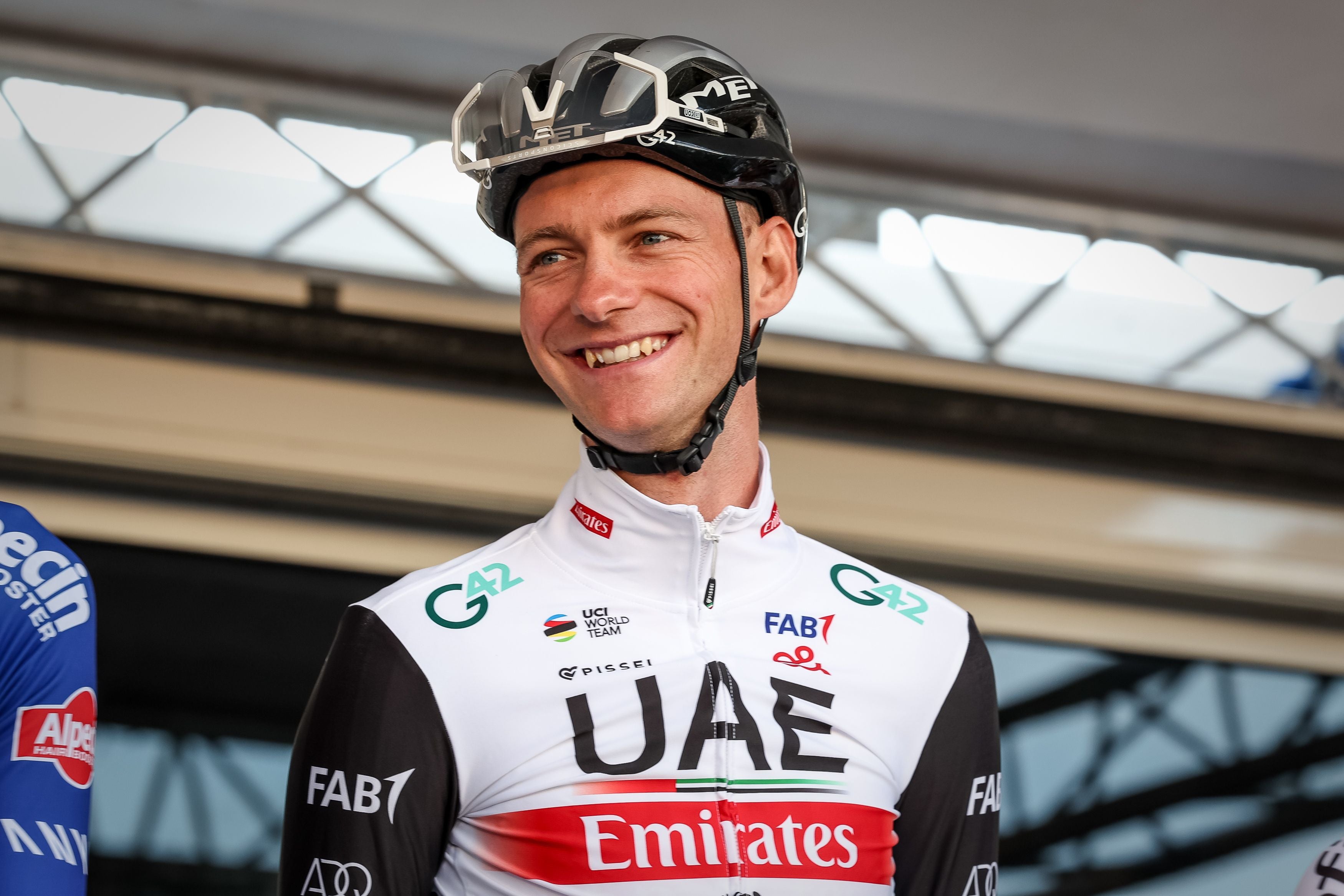 Radrennfahrer Felix Großschartner im weiß-schwarzen UAE Team Emirates Trikot lächelt mit Helm auf dem Podium.