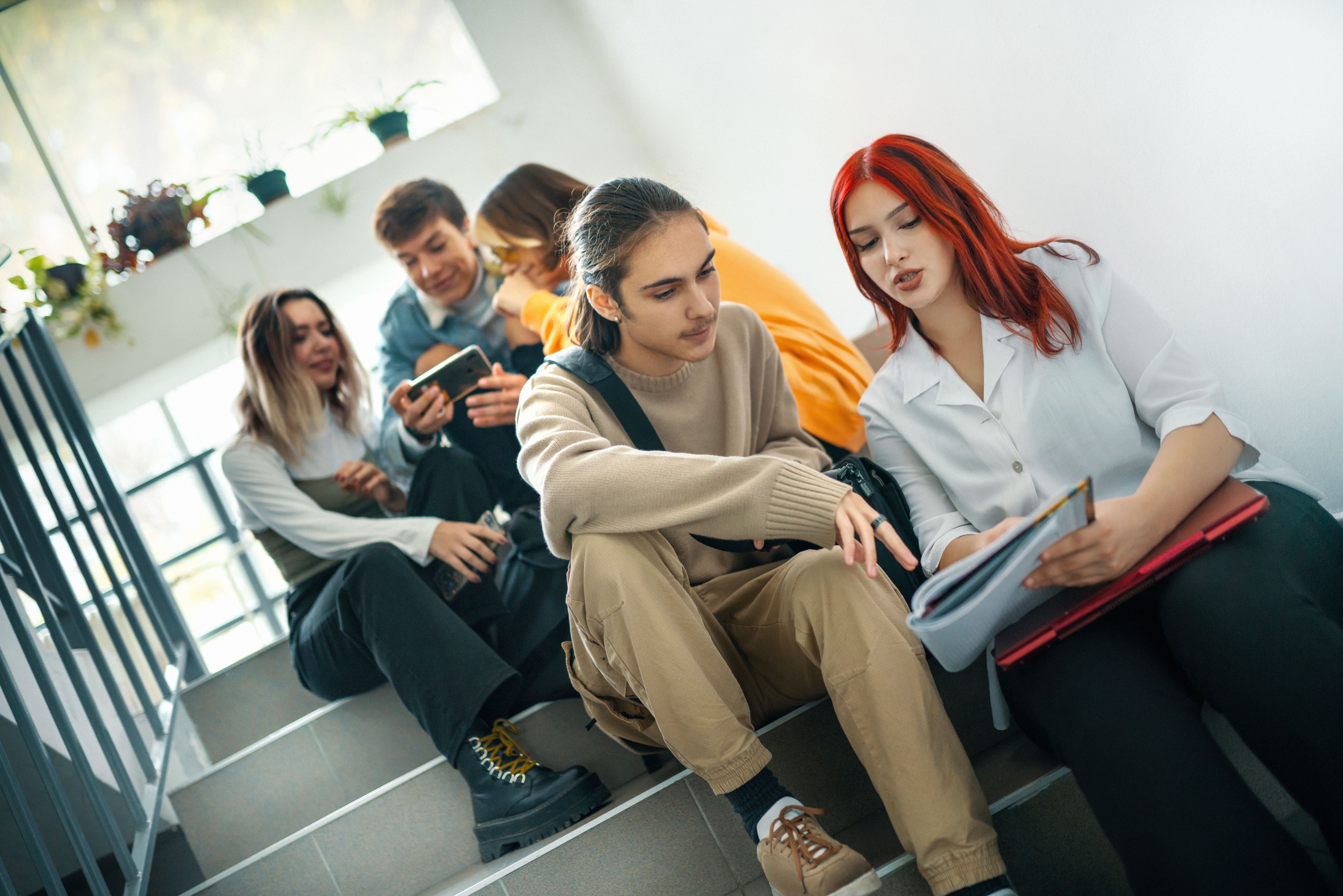 Mehrere Schüler sitzen entspannt auf einer Treppe und unterhalten sich während einer Pause.