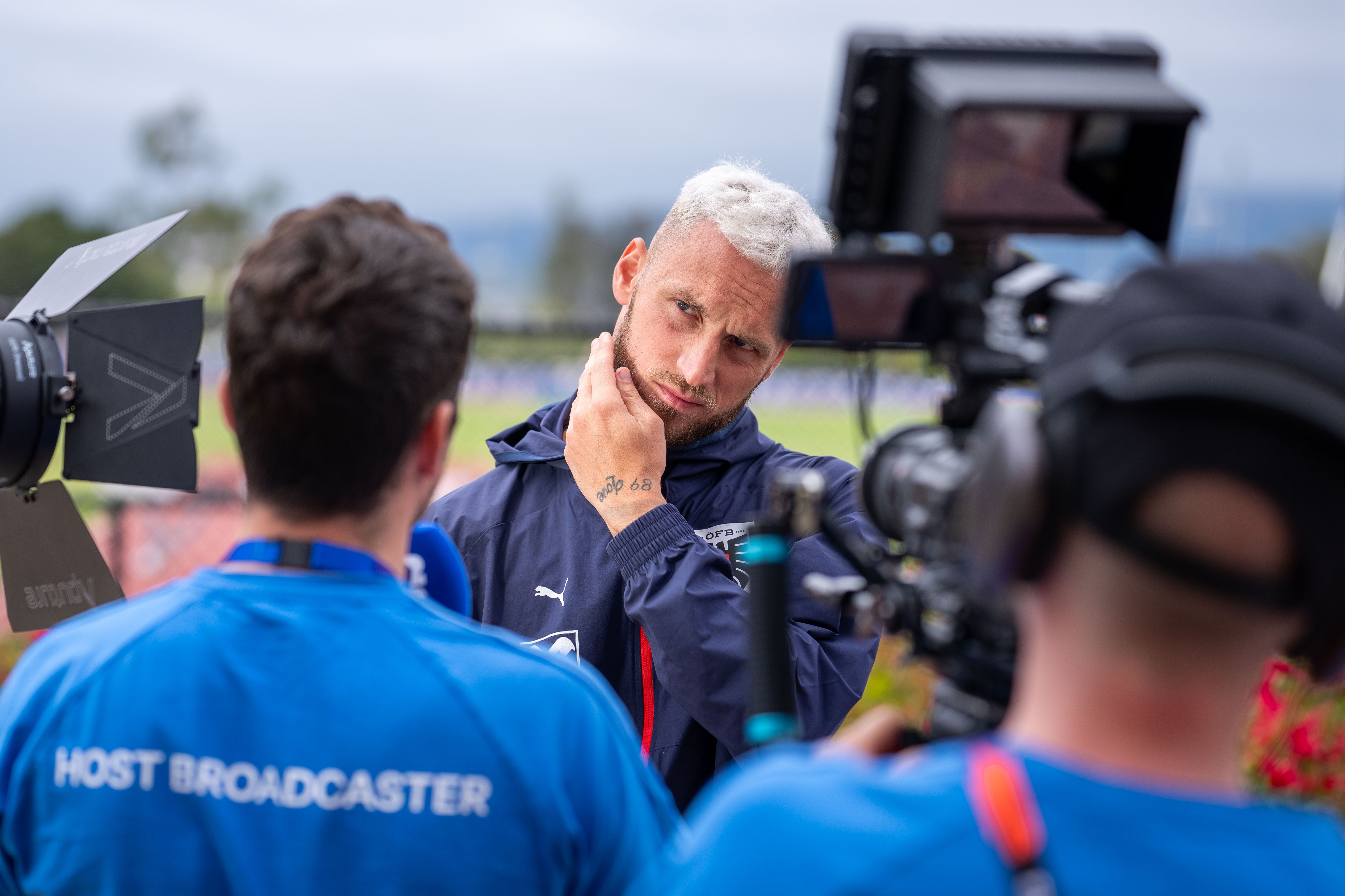 Eine TV-Crew filmt ein Interview mit einer Person im Freien, im Hintergrund unscharfe Natur.