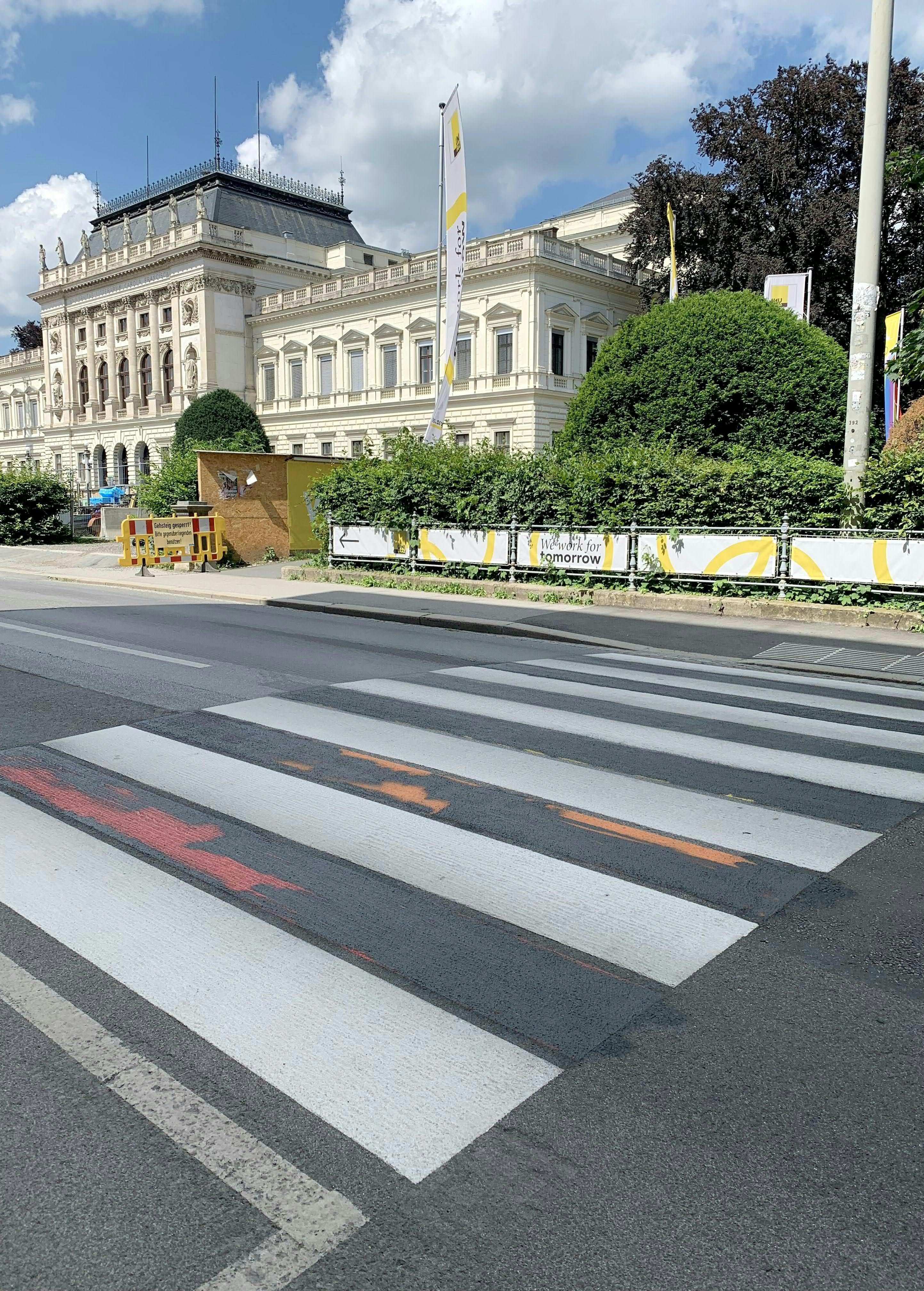 Ein schwarz übermalter Zebrastreifen vor der Karl-Franzens-Universität Graz bei Tageslicht.