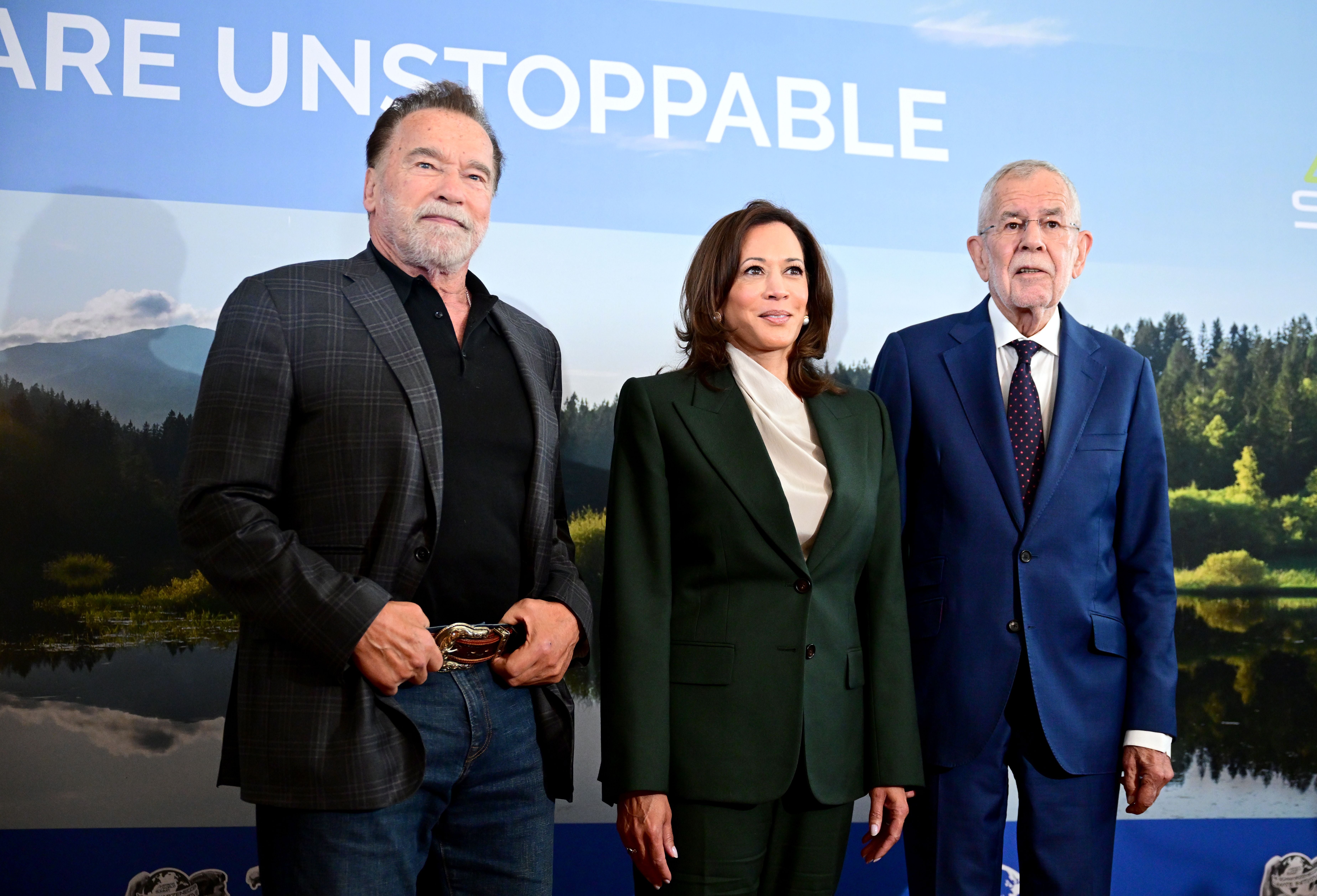 Drei Personen im Anzug stehen vor einer Wand mit der Aufschrift "ARE UNSTOPPABLE".