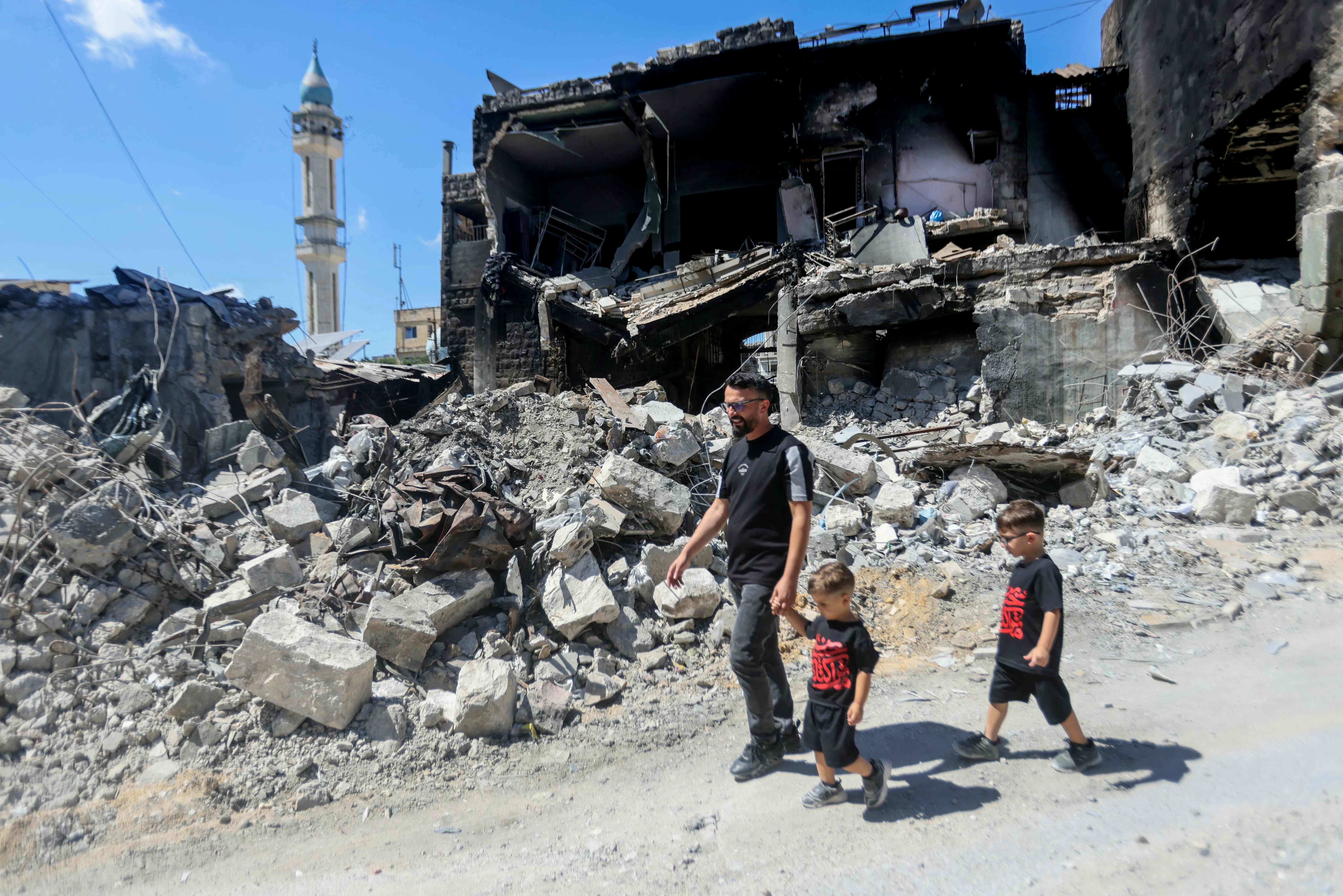 TOPSHOT - A man walks with his children past a destroyed building after returning to the southern Lebanese village of Nabatieh on June 18, 2026. The Israeli military said on June 18 it will continue operating in southern Lebanon and 'remove threats' beyond its so-called security zone, after the US and Iran signed an agreement to end the Middle East war, including in Lebanon. (Photo by MAHMOUD ZAYYAT / AFP) /