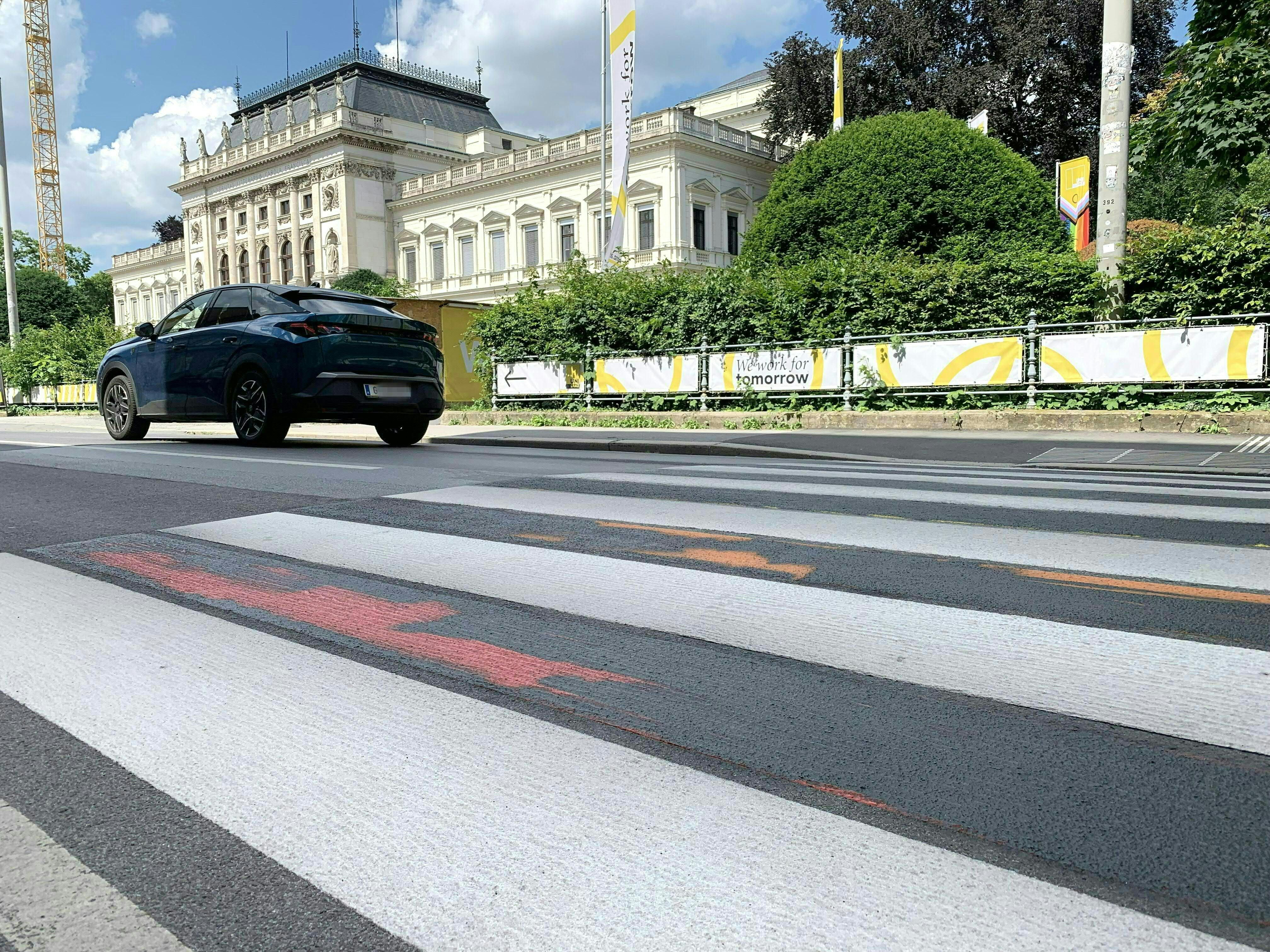 Ein übermalter Zebrastreifen vor der Karl-Franzens-Universität Graz, daneben ein parkendes Auto.
