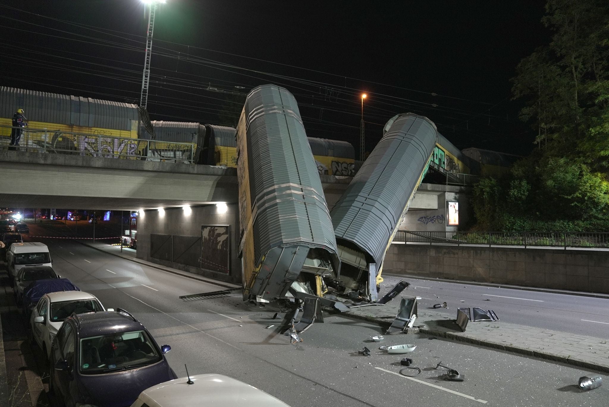 Zwei Güterzugwaggons liegen nach einem Brückensturz zerstört auf einer Straße bei Nacht.