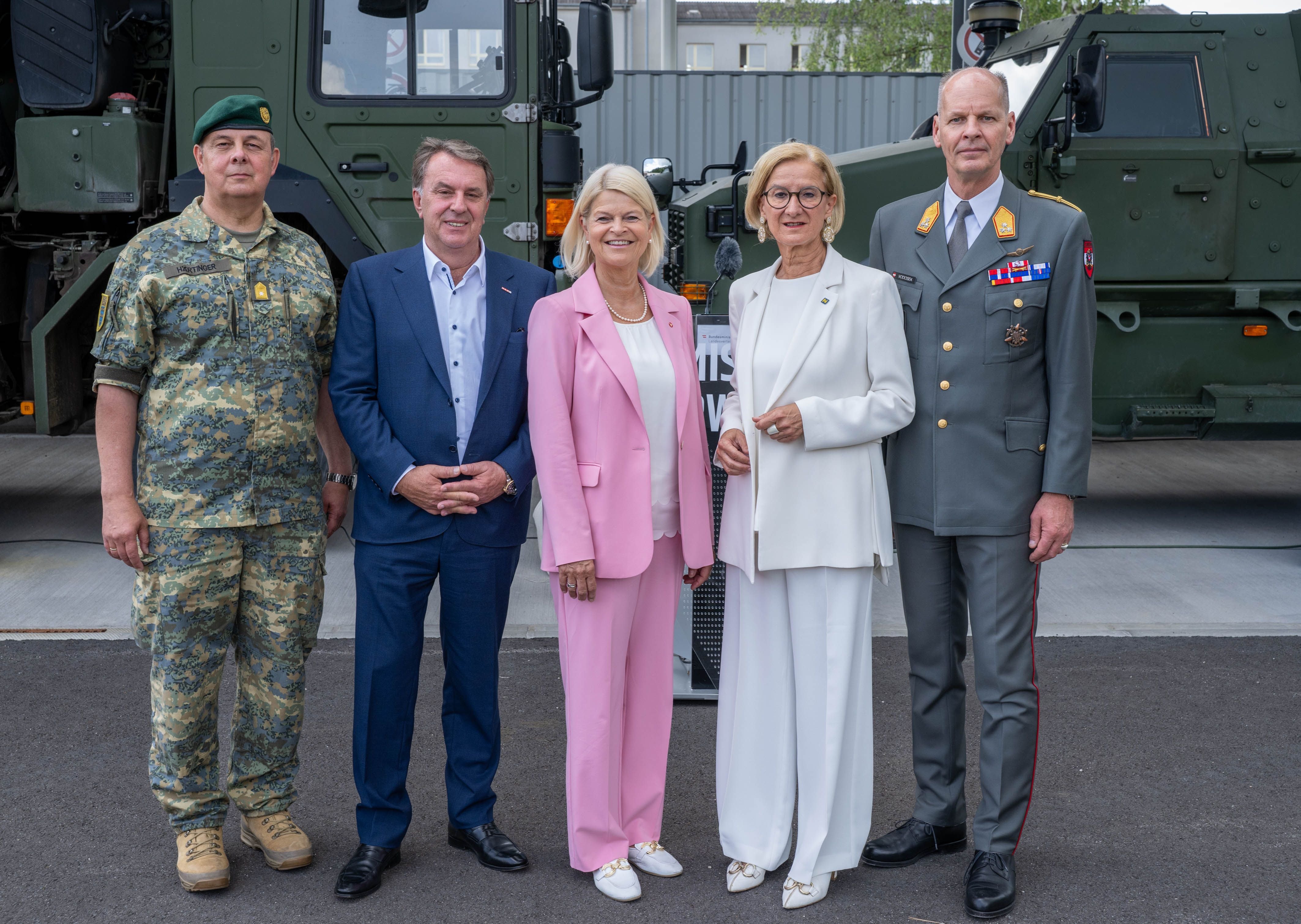 Fünf Personen posieren nach einer Pressekonferenz vor zwei Militärfahrzeugen.