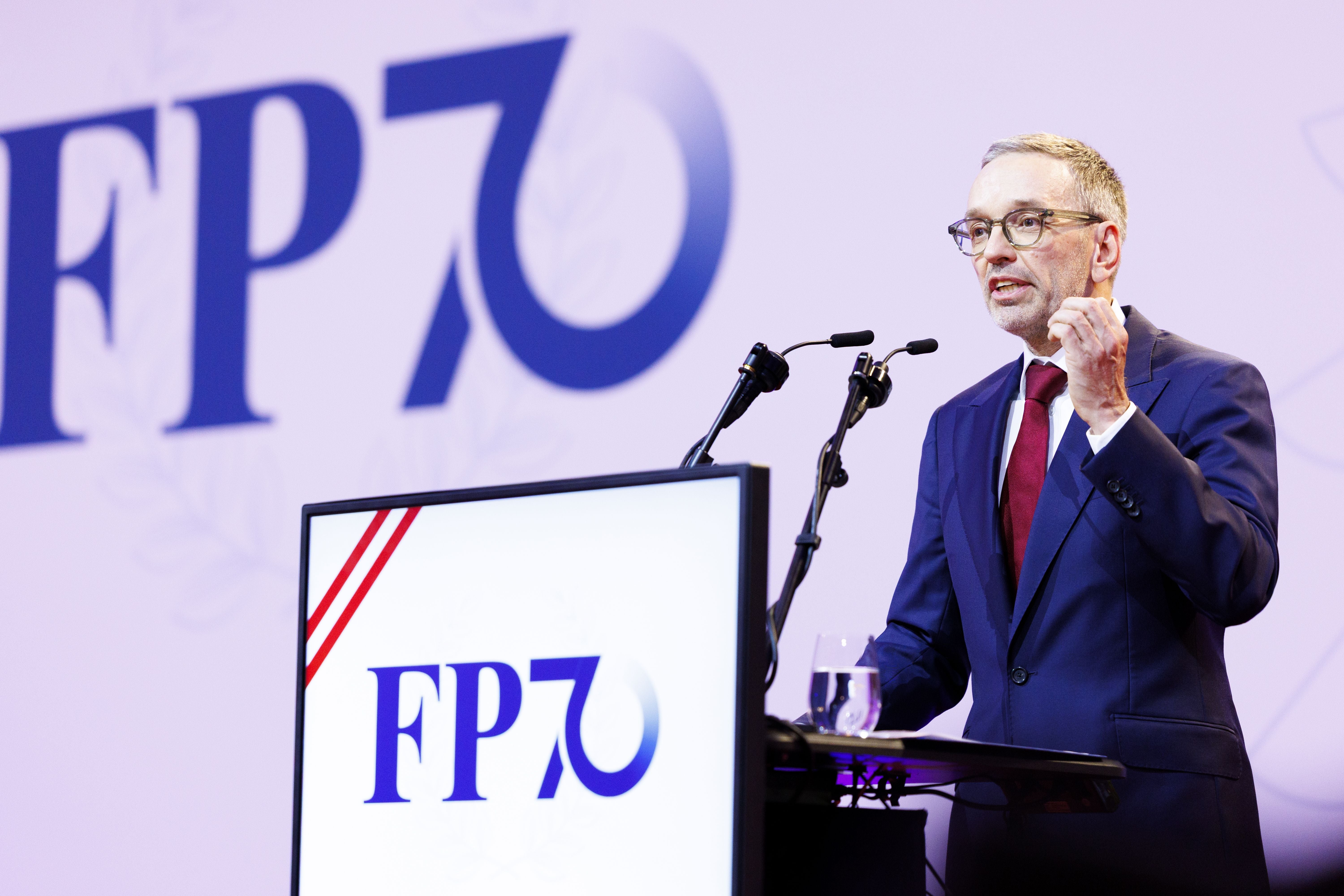 Ein Mann im Anzug spricht bei einer Veranstaltung der FPÖ an einem Rednerpult mit Mikrofonen.