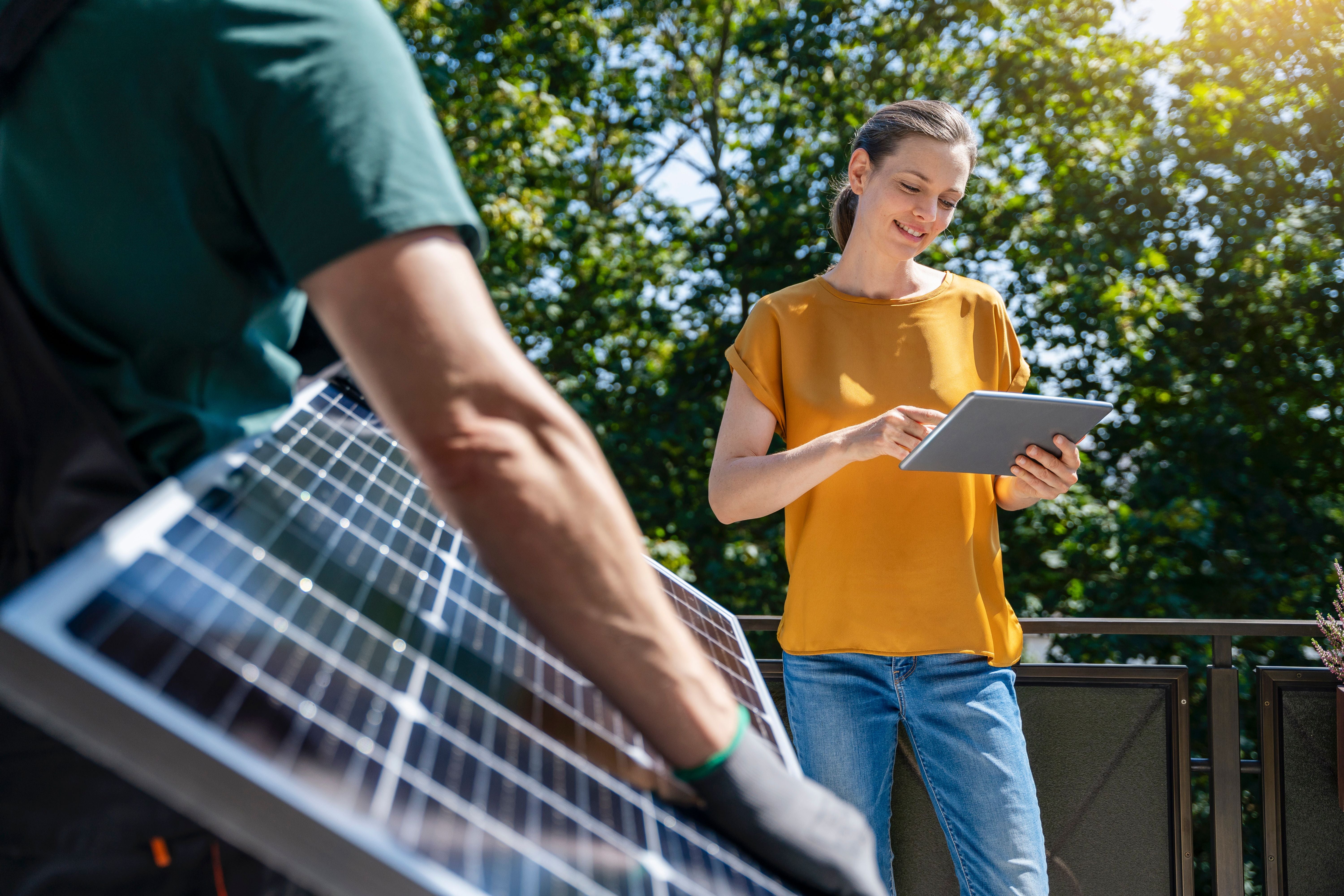 Eine Frau bedient ein Tablet, während eine Person ein Solarmodul im Freien hält.