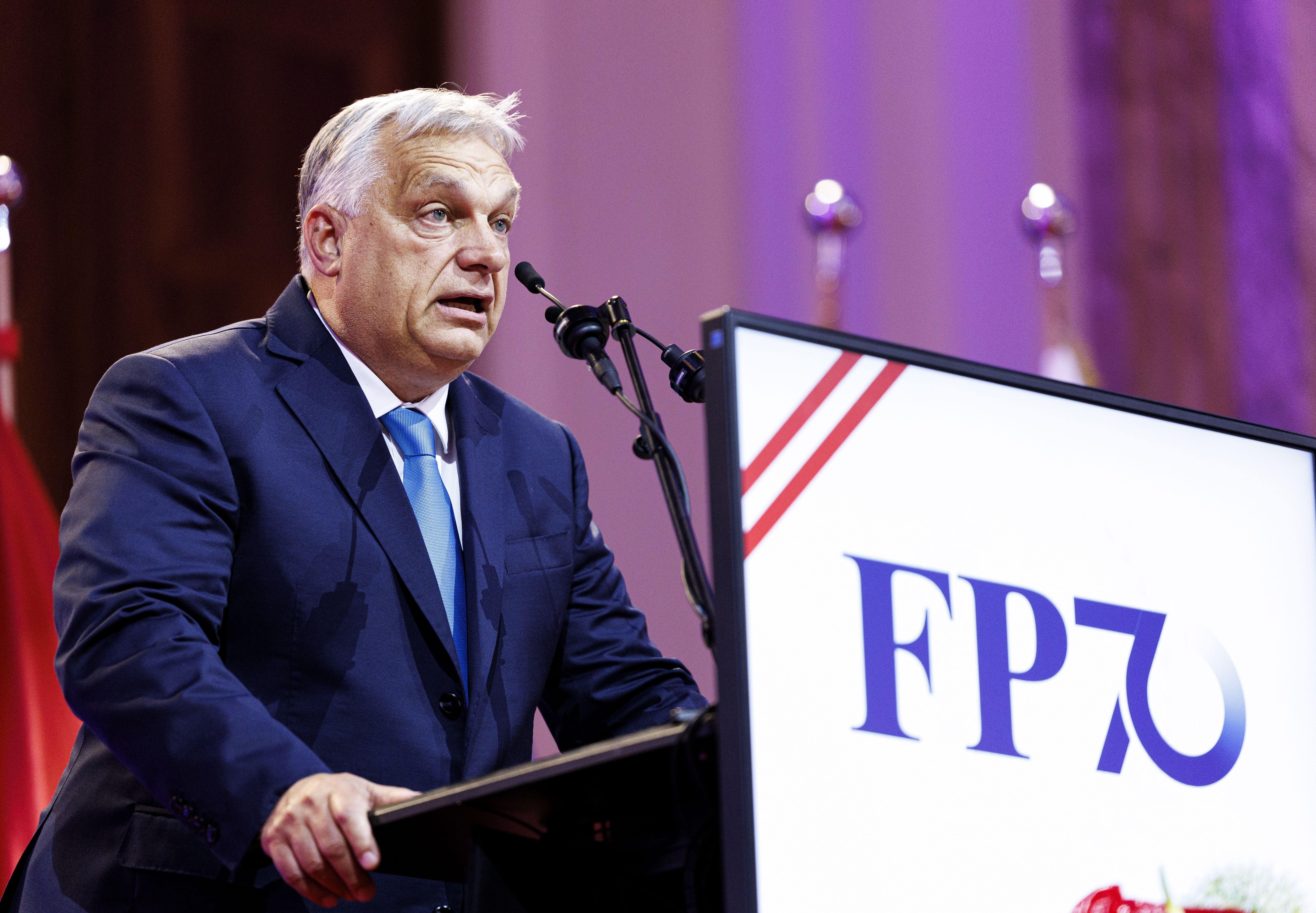 Ein Mann im Anzug spricht am Rednerpult mit FPÖ 70-Logo bei einer Veranstaltung.