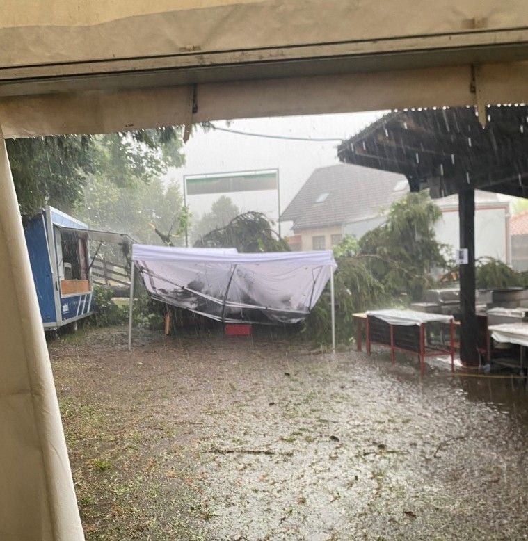 Starker Regen und umgestürzte Bäume bei einem Festgelände, zerstörtes Zelt im Vordergrund.