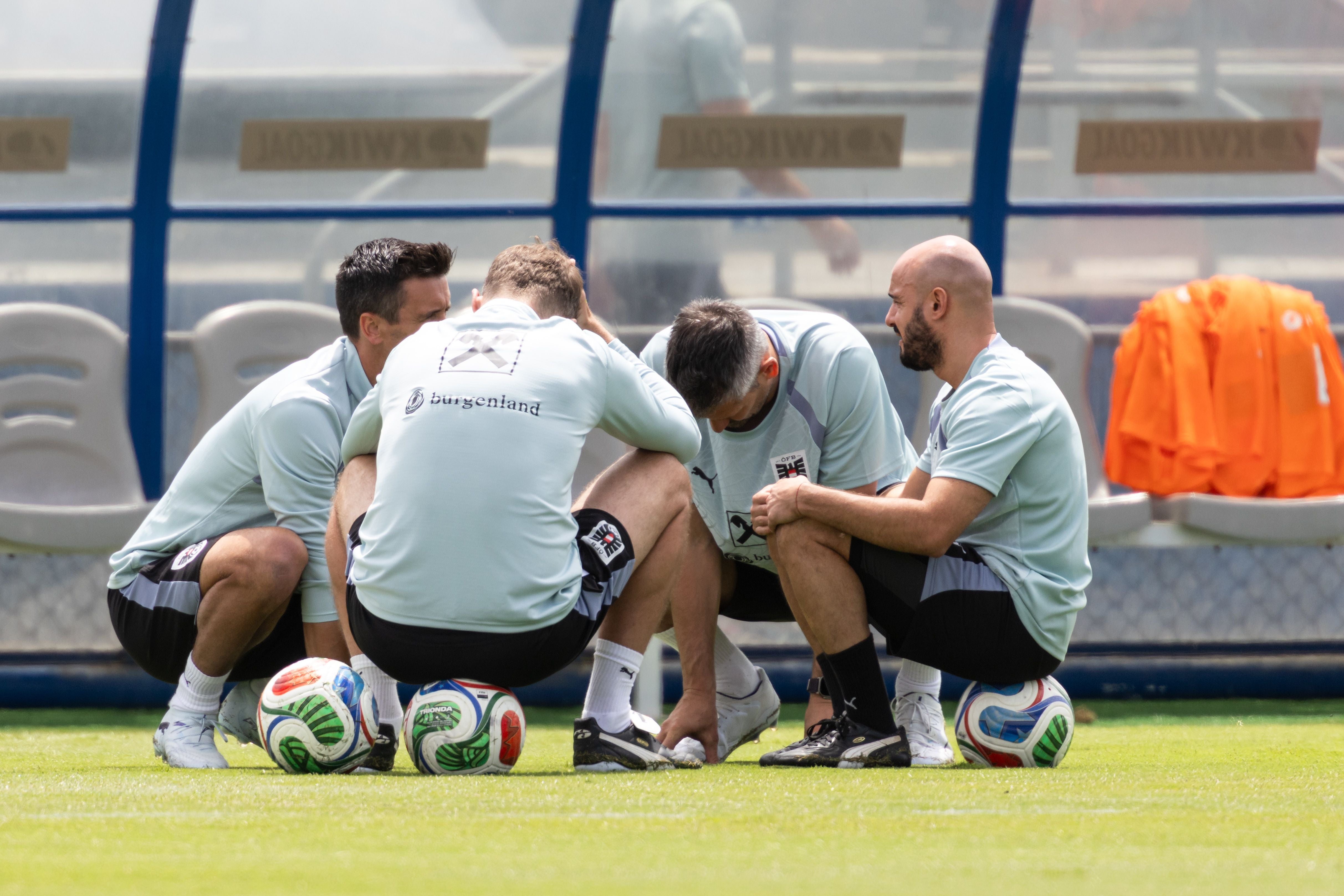 Vier Fußballtrainer des österreichischen Teams hocken im Kreis auf dem Spielfeld und besprechen sich.