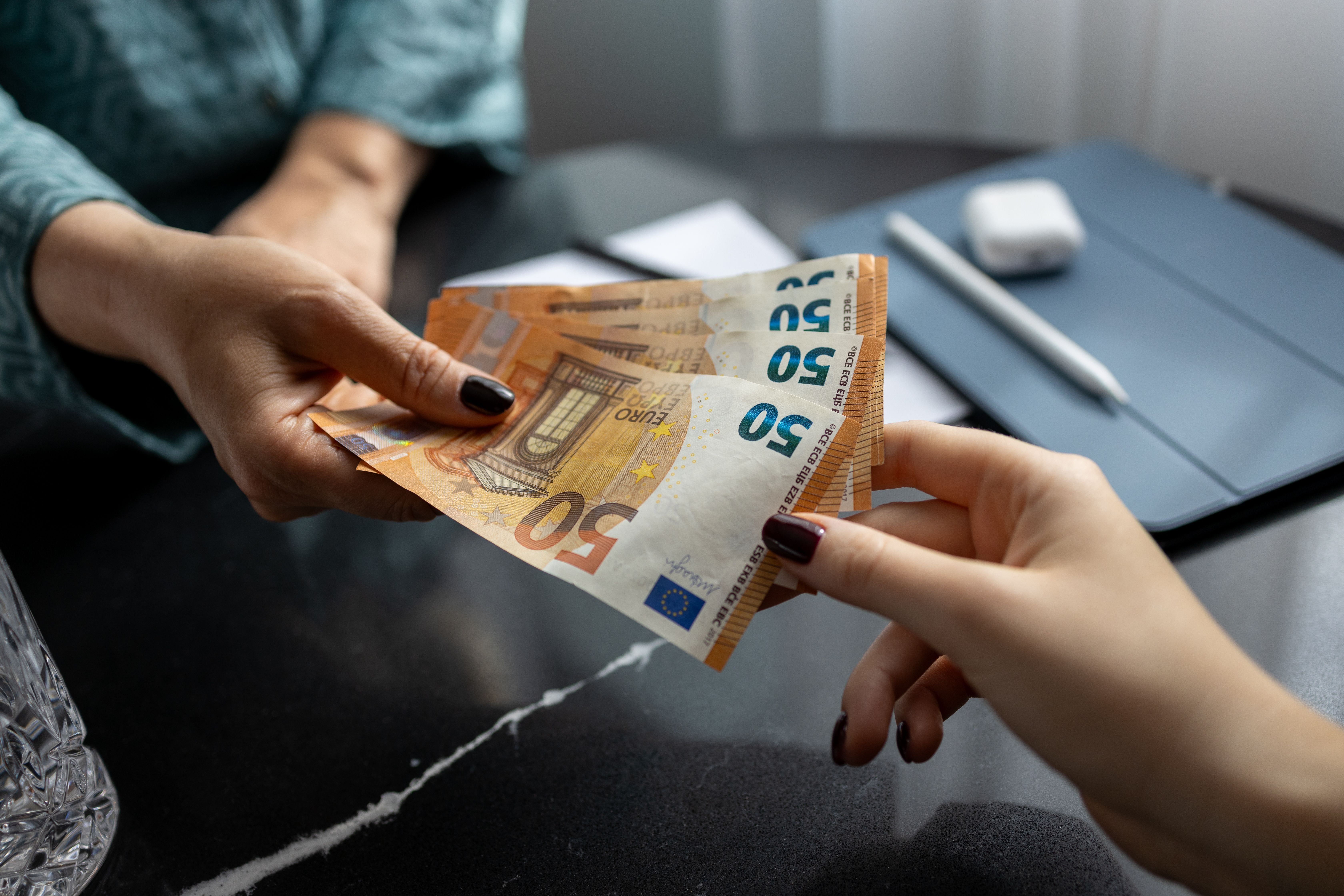 Zwei Frauen tauschen mehrere 50-Euro-Scheine an einem Tisch.