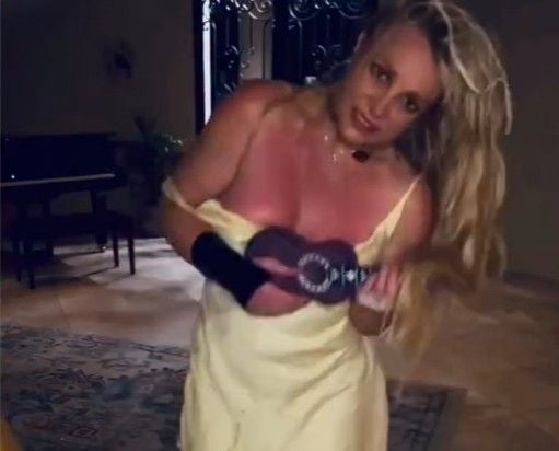 Britney Spears im gelben Kleid mit Sonnenbrand spielt drinnen eine Ukulele.