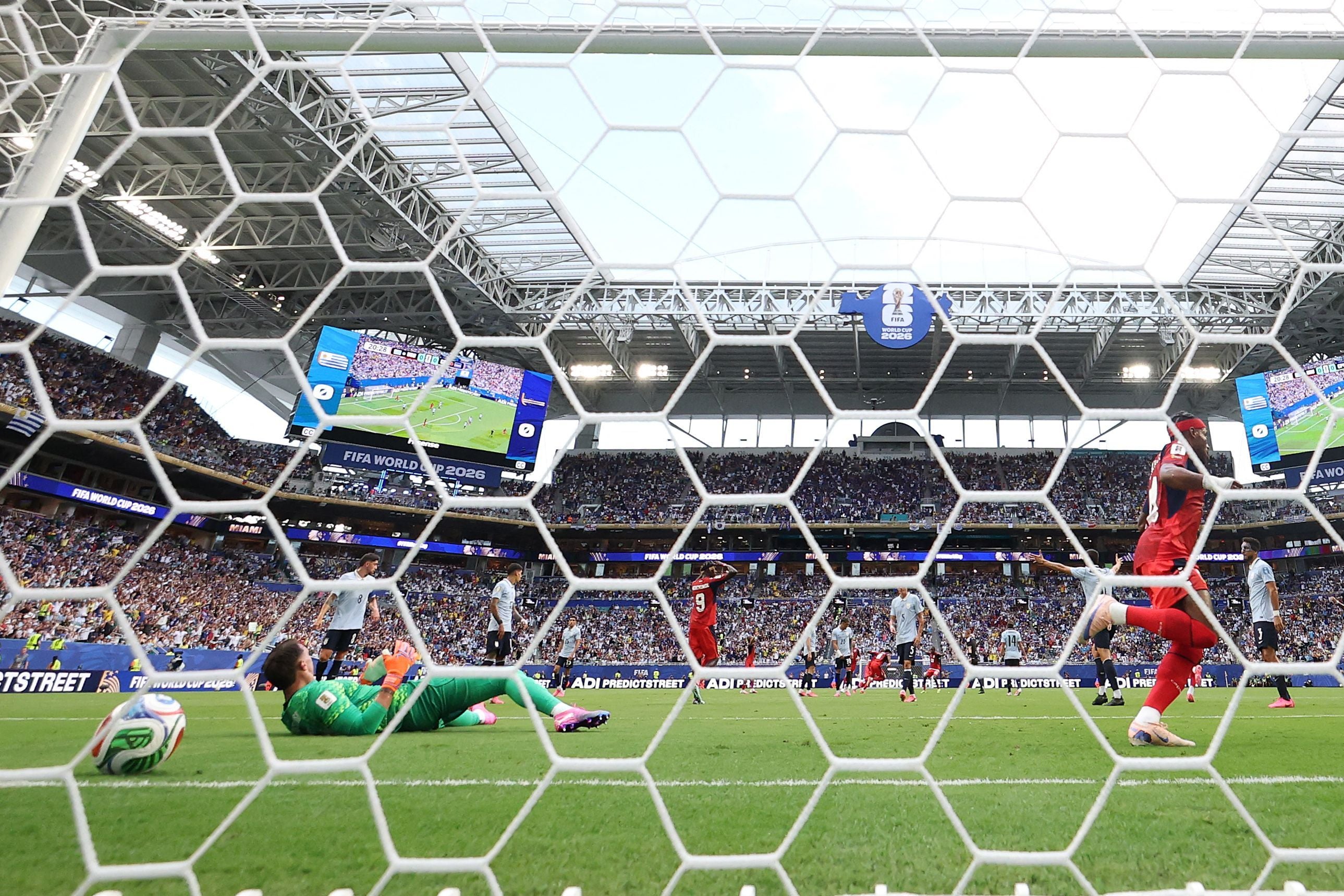 Ein Fußballtorwart liegt am Boden, der Ball im Netz, Fans jubeln im vollen Stadion.