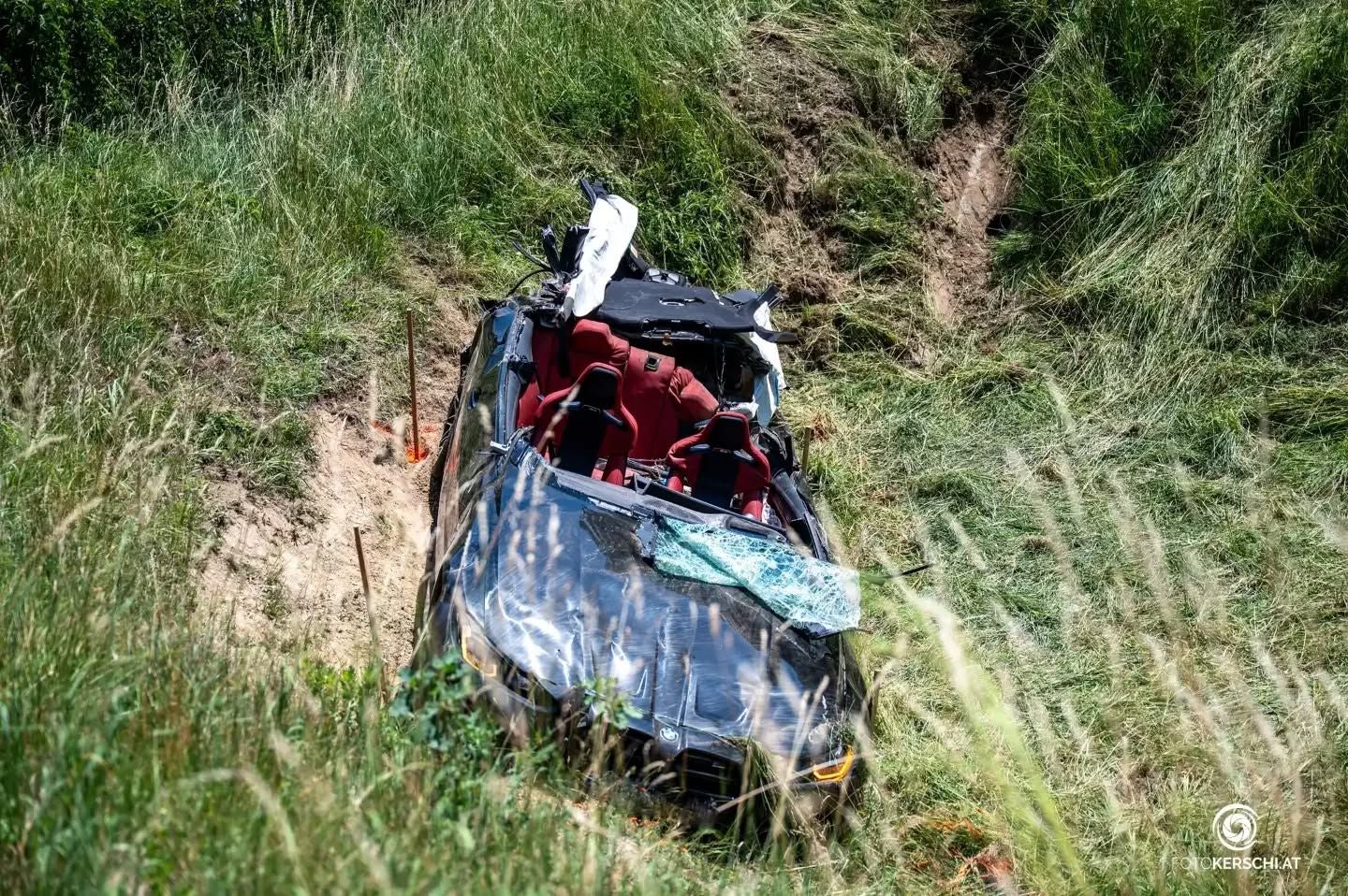 Ein stark beschädigtes Auto liegt im hohen Gras neben einer Böschung, Airbag und Glassplitter sichtbar.