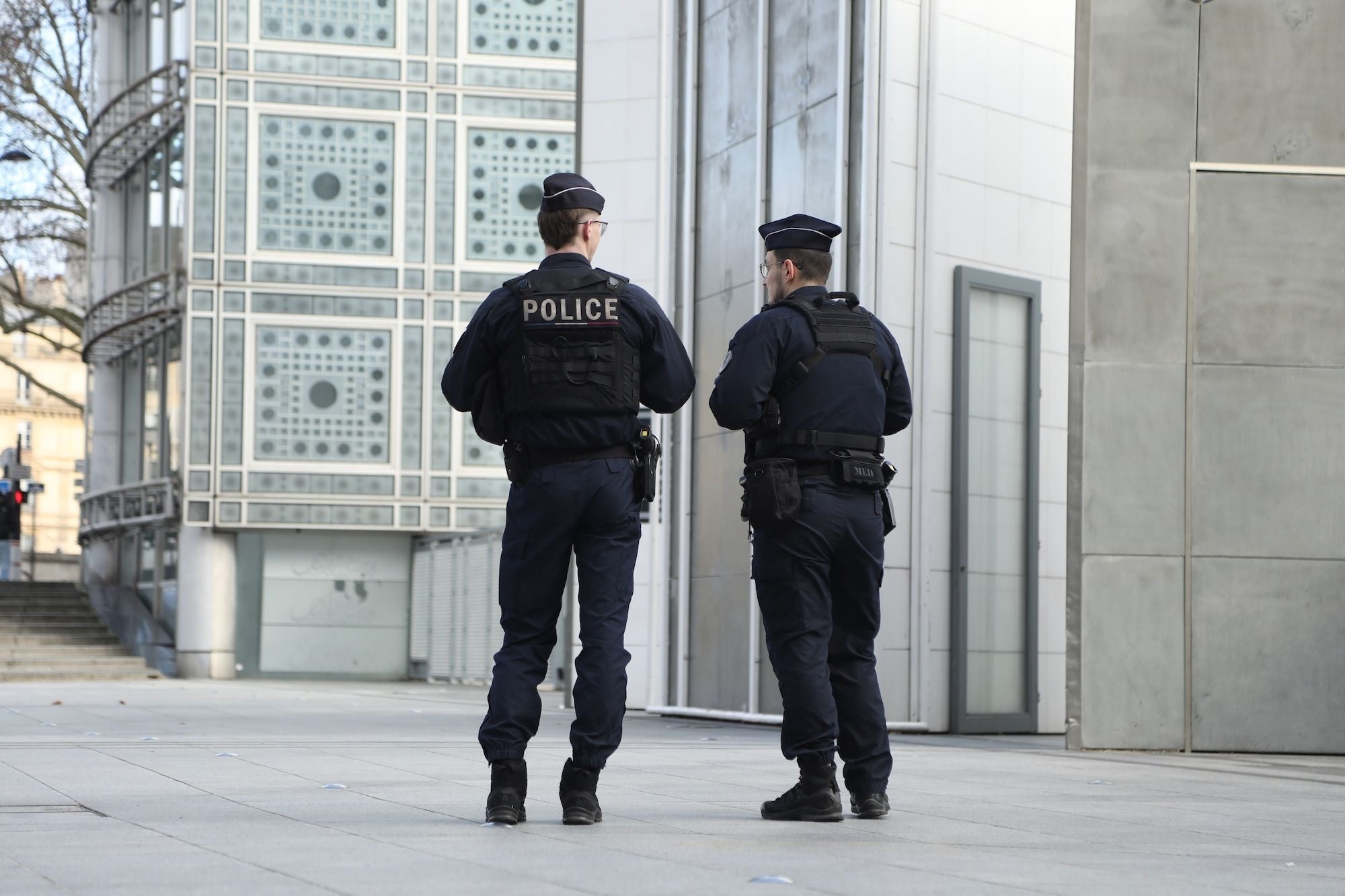 Zwei Polizisten in Uniform gehen vor einem modernen Gebäude in einer Stadt spazieren.