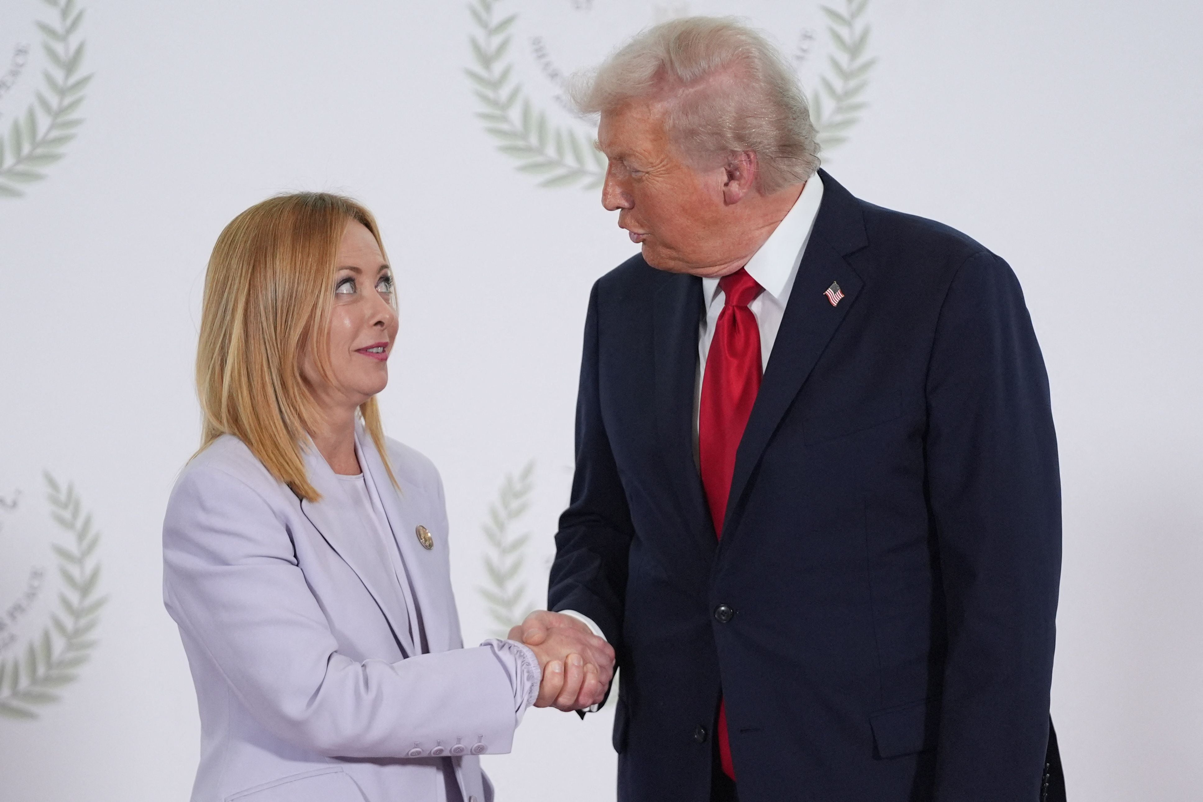 Ein Mann und eine Frau im Anzug geben sich vor weißem Hintergrund die Hand.