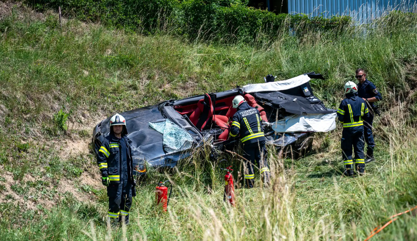 Feuerwehrleute stehen bei einem Autowrack im Gras am Hang nach einem Unfall.
