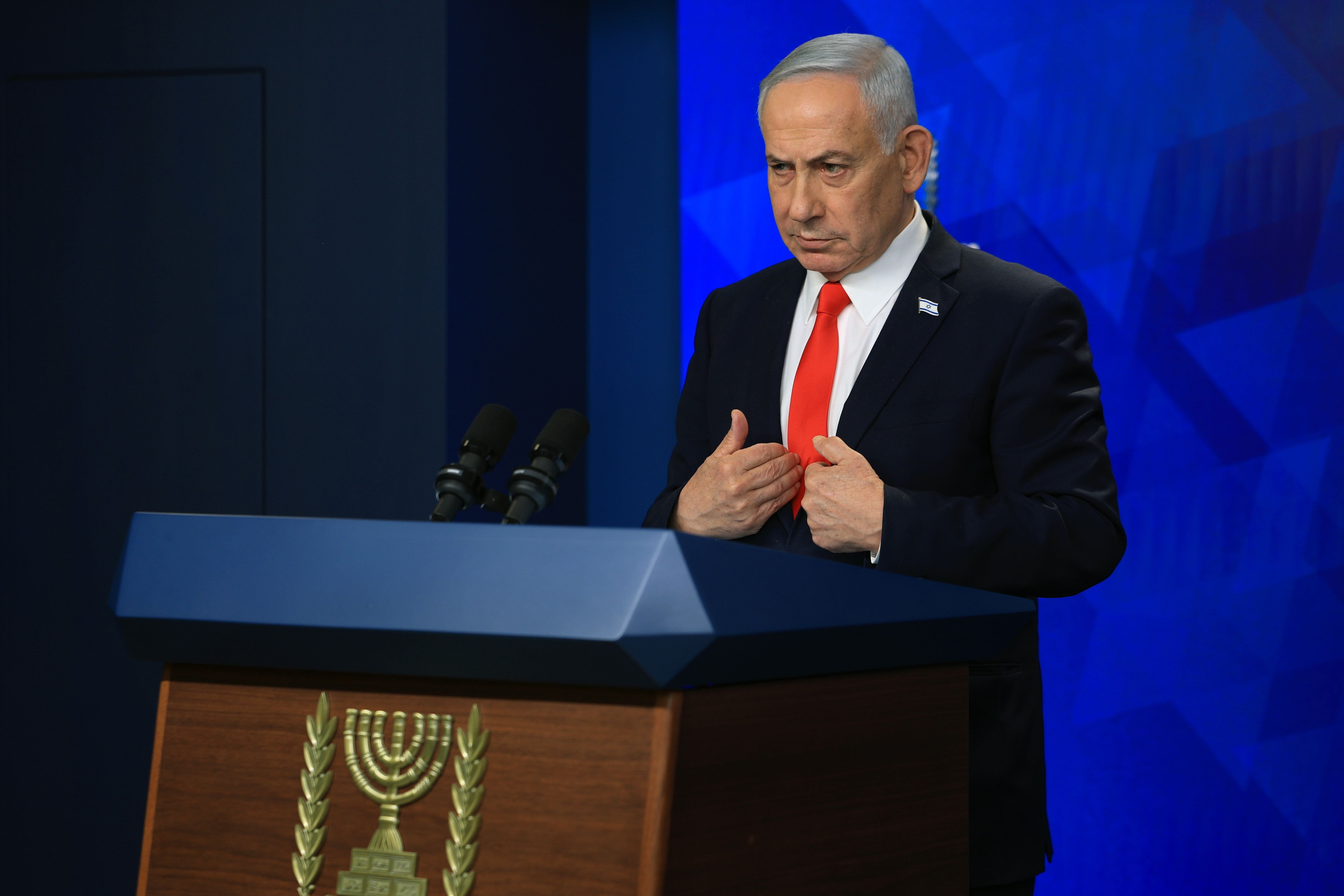Ein Mann im Anzug spricht an einem Rednerpult mit dem Emblem Israels vor blauem Hintergrund.