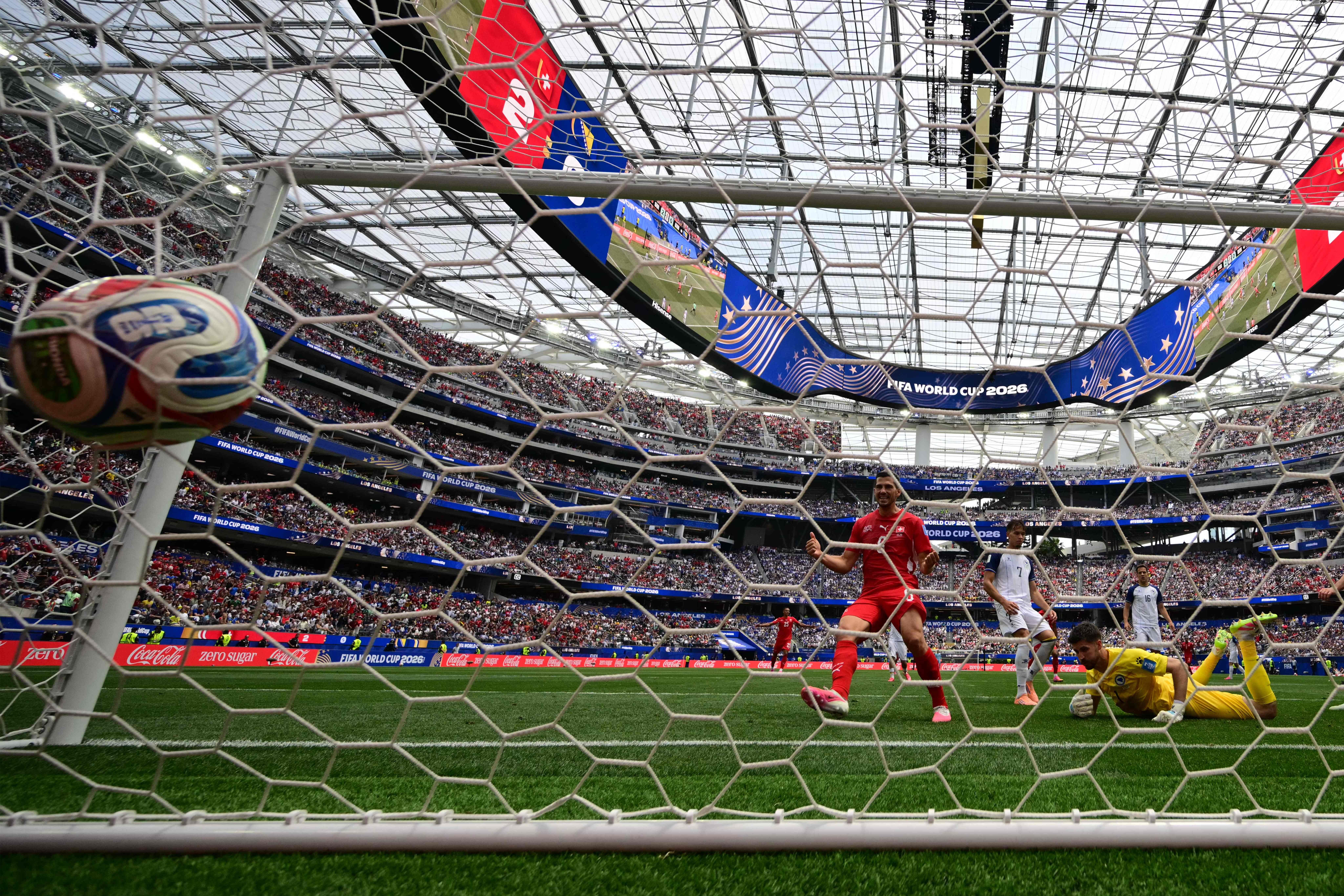 Ein Fußball fliegt ins Tor während eines WM-Spiels im vollen Stadion, Spieler jubeln.