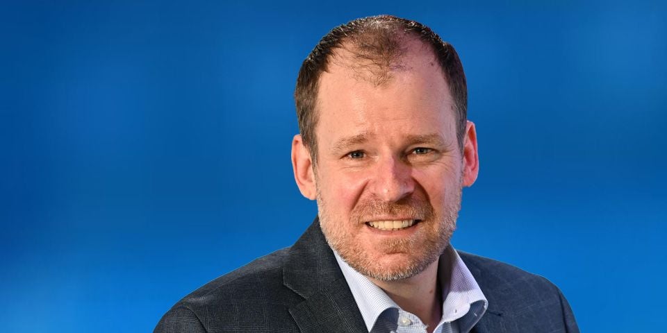 Ein Mann im Anzug vor blauem Hintergrund, sein Gesicht ist unscharf gemacht.