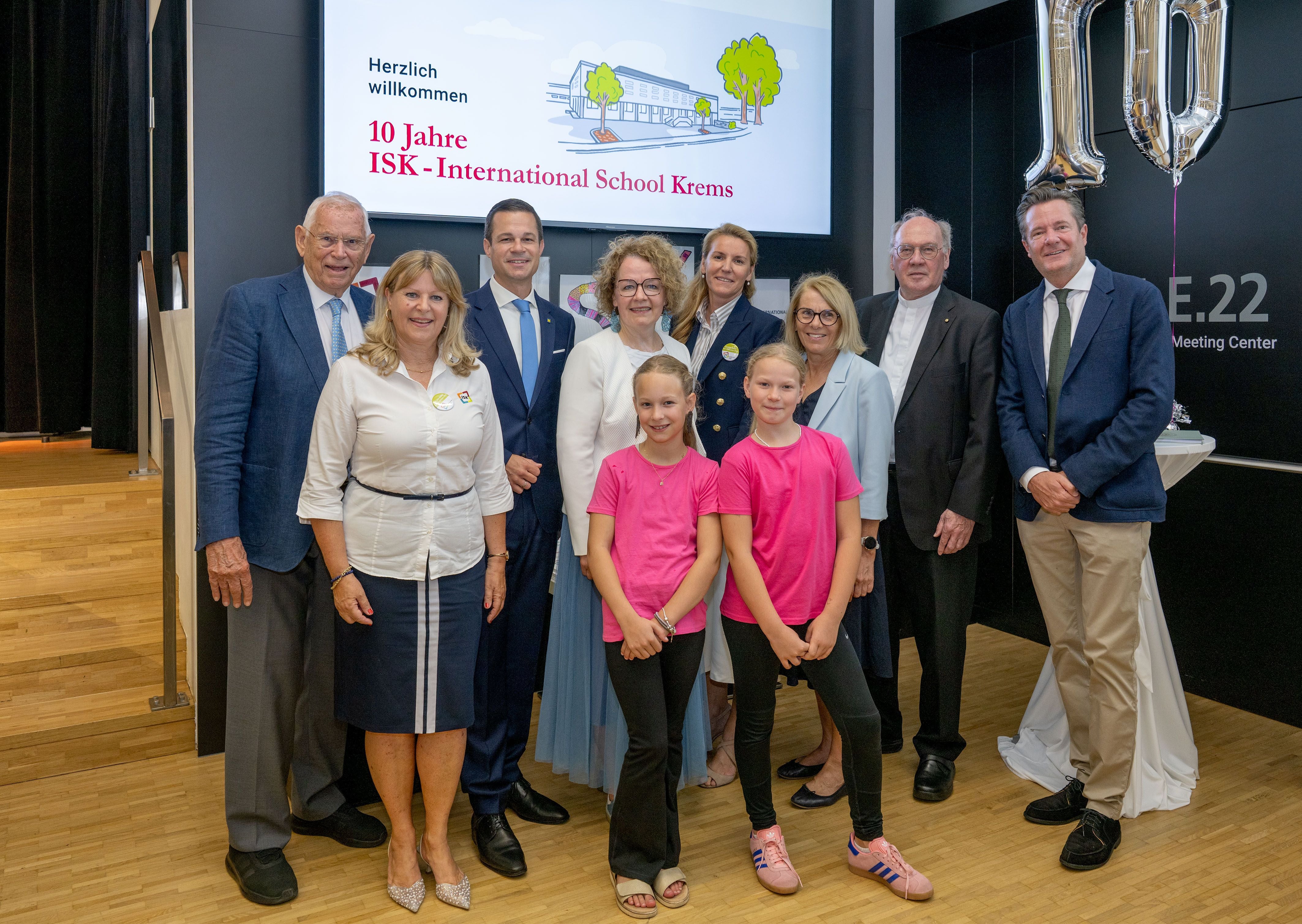 Gruppenfoto von Erwachsenen in Businesskleidung und zwei Schülerinnen in pinken T-Shirts.