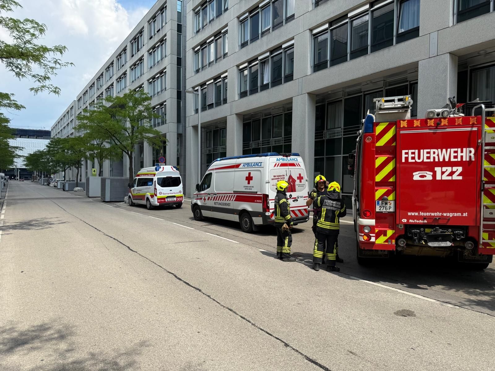 Feuerwehr- und Rettungsfahrzeuge vor einem Gebäude, Feuerwehrleute stehen neben dem Einsatzwagen.