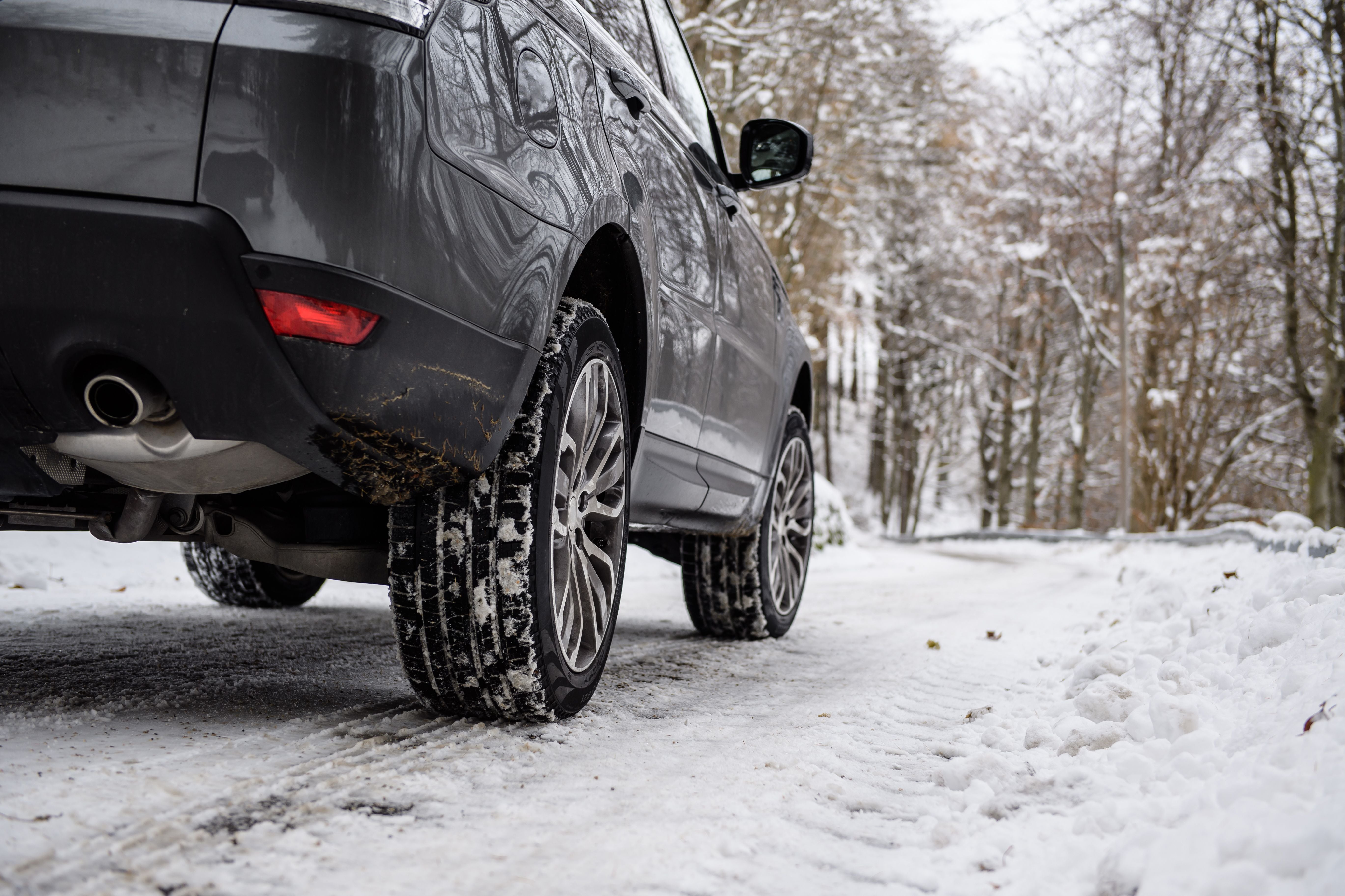 Auto mit Winterreifen fährt auf verschneiter Straße durch bewaldete Winterlandschaft.