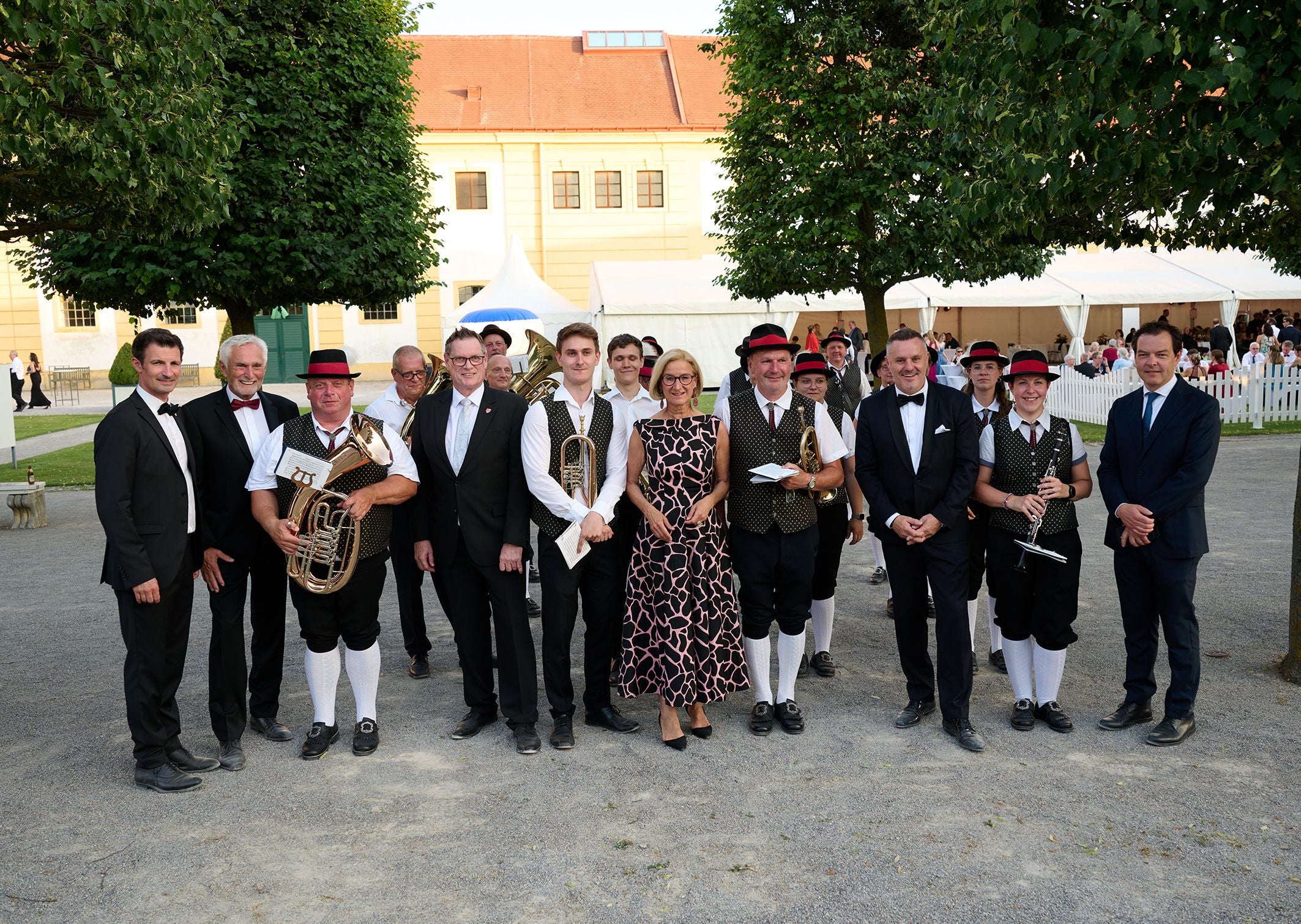 Gruppe von Menschen, teils in Tracht, posiert im Freien vor einem Festzelt für ein Foto.