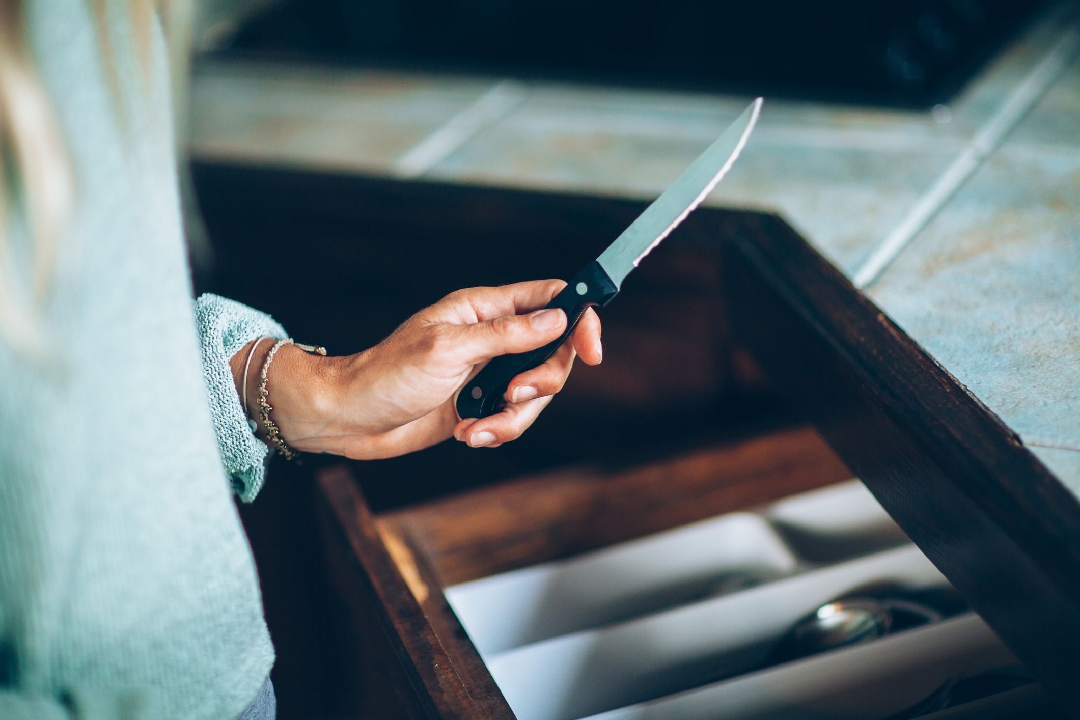 Nahaufnahme einer Hand, die ein Messer vor einer offenen Küchenschublade hält.