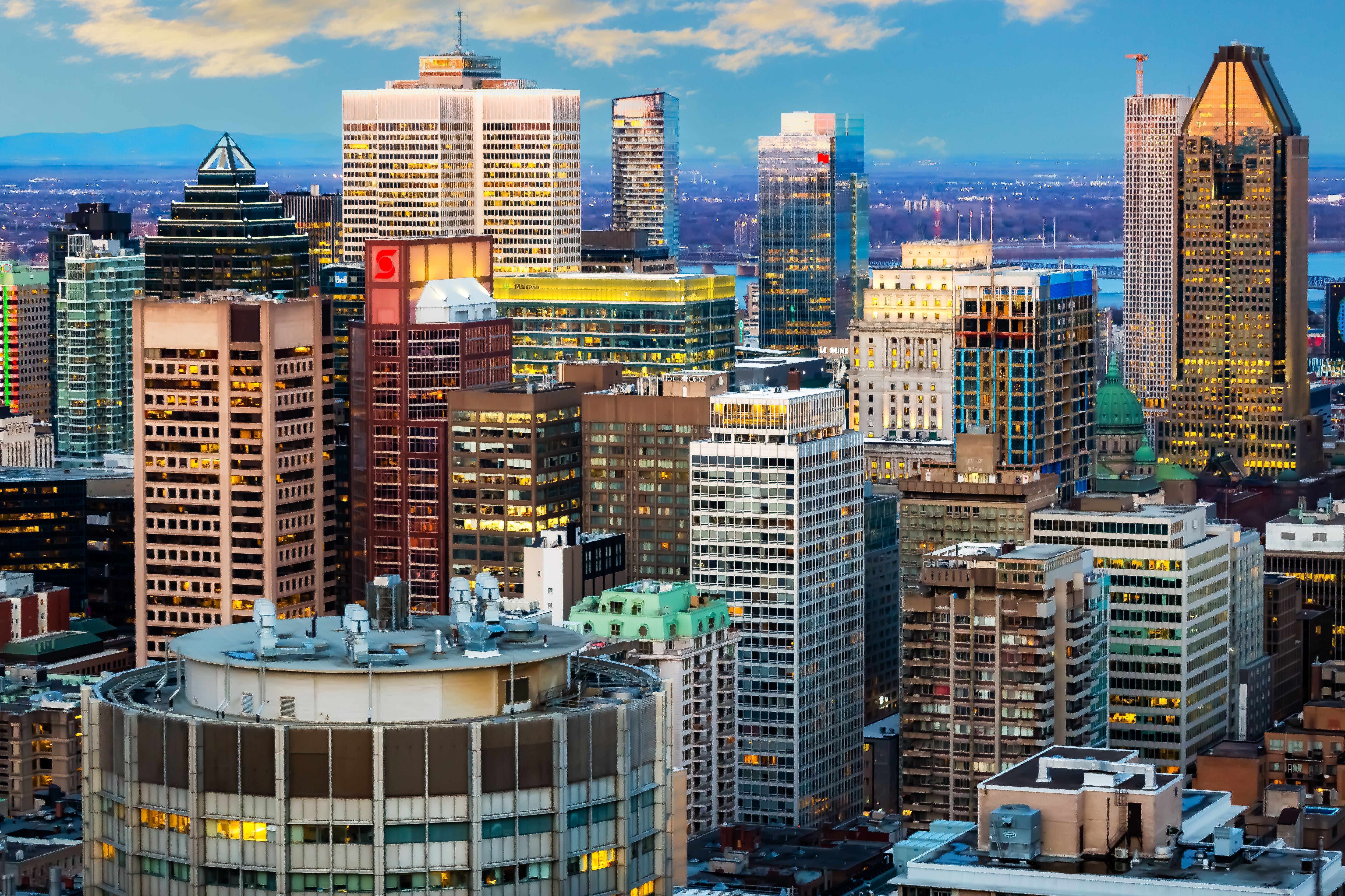 Montreals Skyline bei Dämmerung, beleuchtete Hochhäuser vor blauem Himmel.
