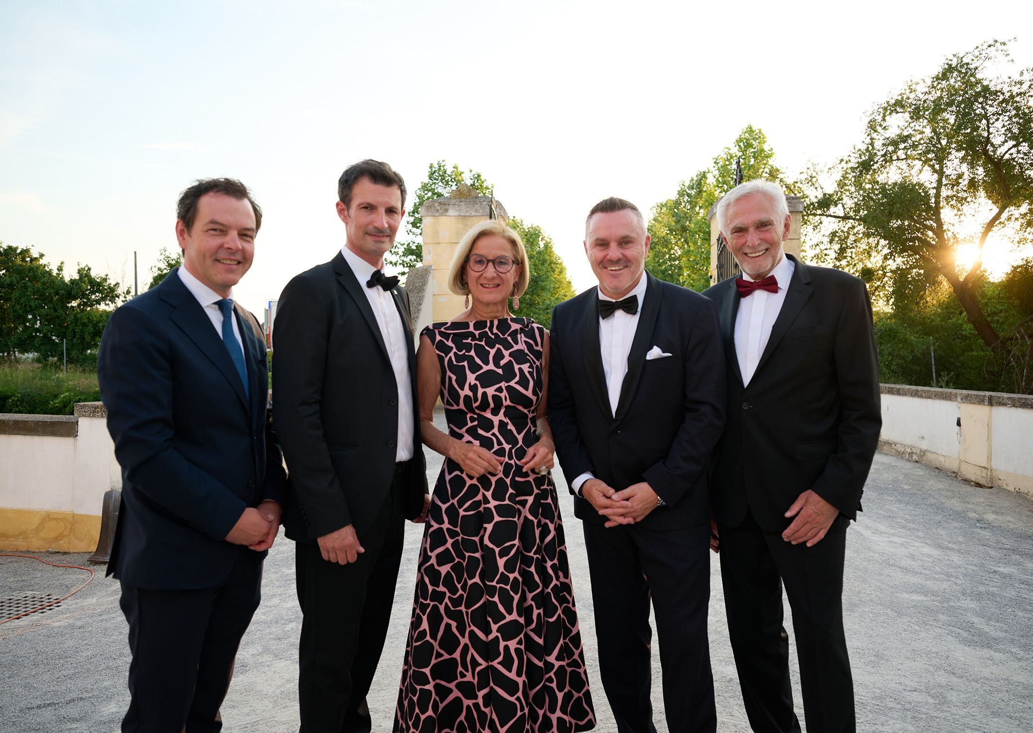 Fünf elegant gekleidete Personen posieren abends im Freien bei einer Veranstaltung.