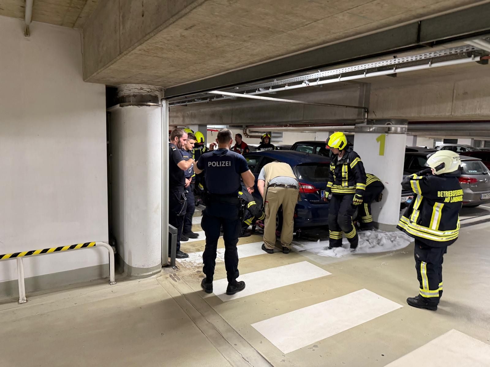 Feuerwehr und Polizei arbeiten gemeinsam an einem Einsatz bei einem Auto in einer Parkgarage.