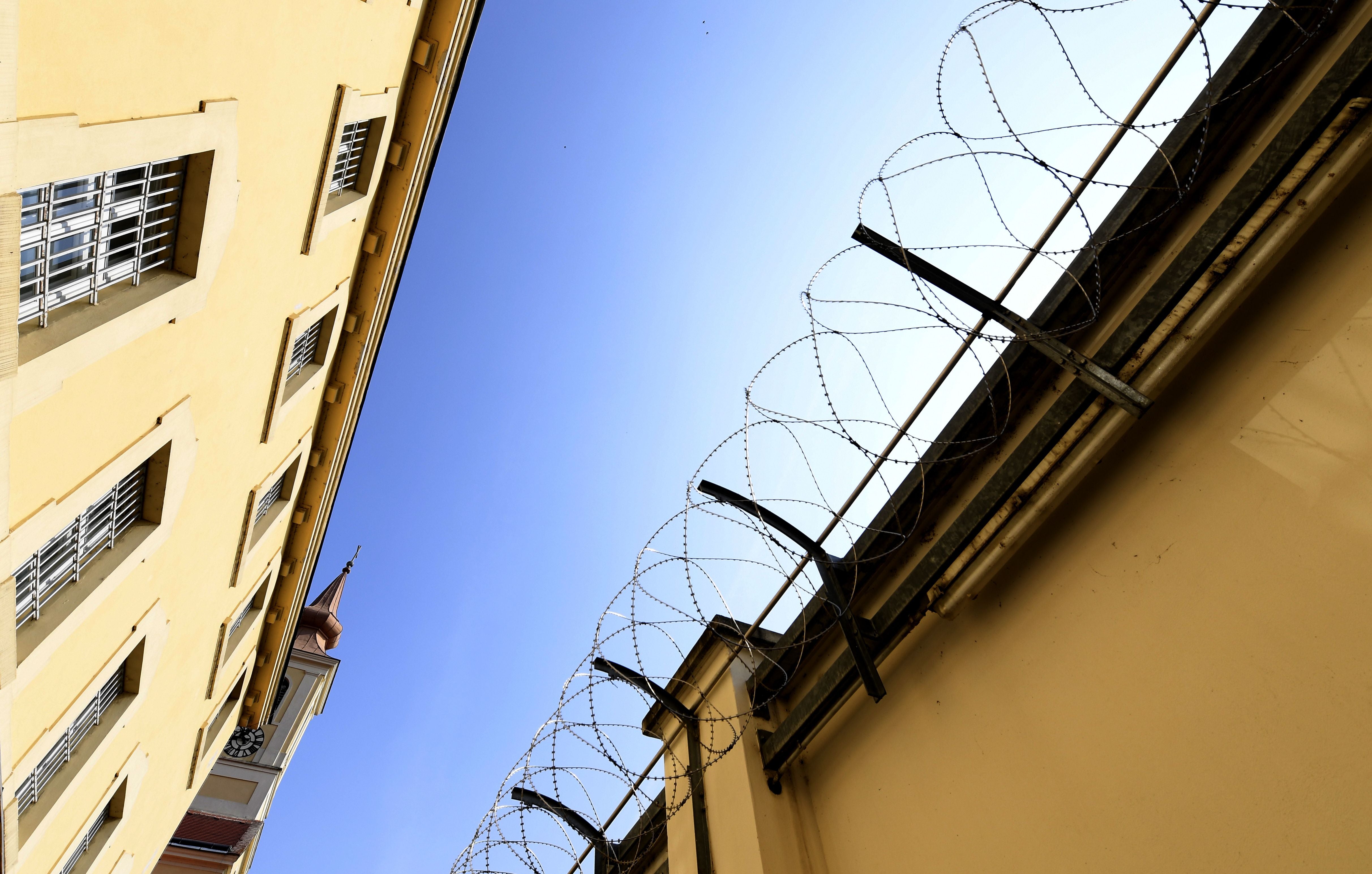 Gefängnismauer mit Stacheldraht und vergitterte Fenster vor blauem Himmel in Stein, Österreich.