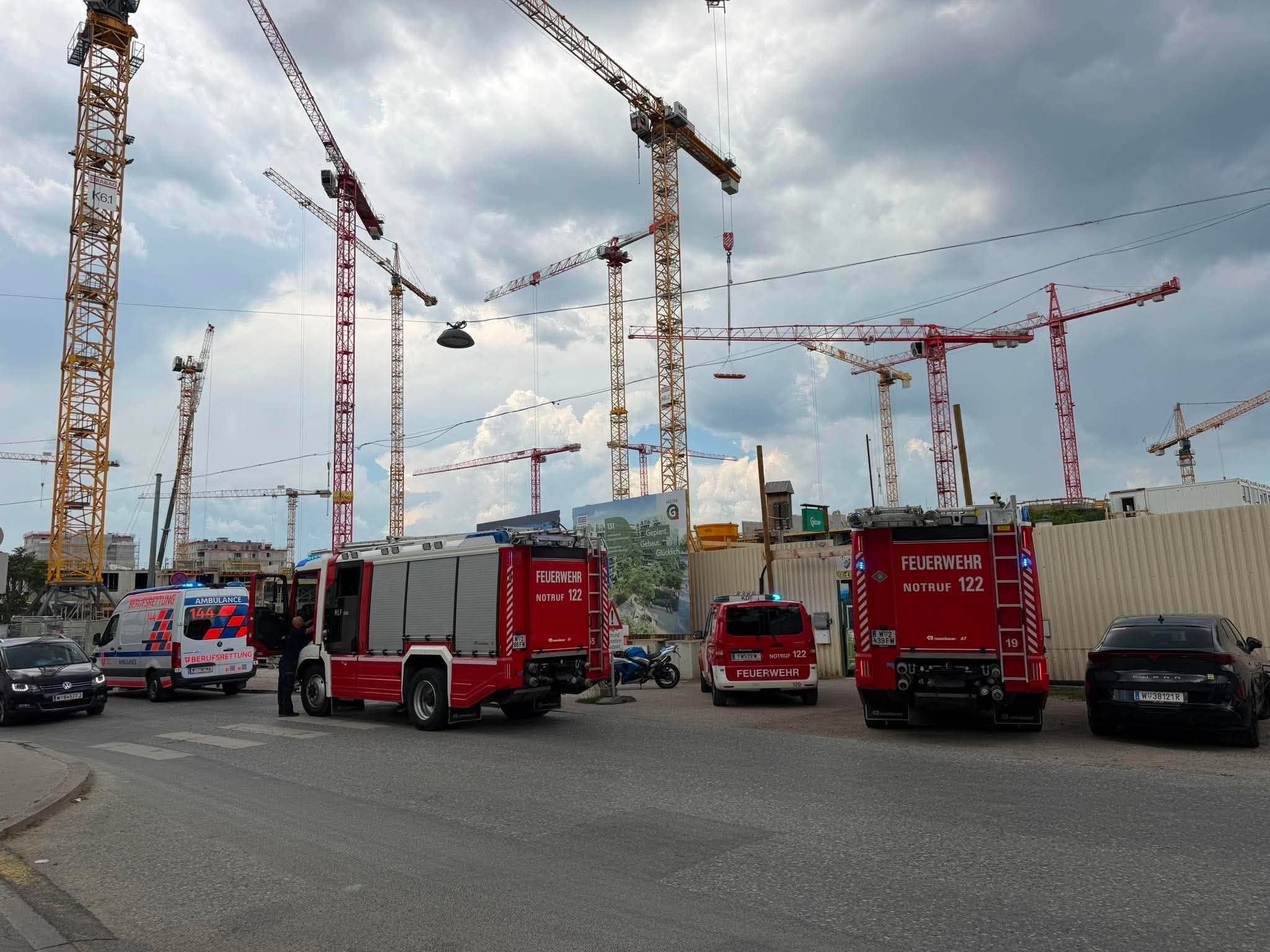 Mehrere Feuerwehr- und Rettungsfahrzeuge stehen bei einem Einsatz auf einer Baustelle mit Baukränen.